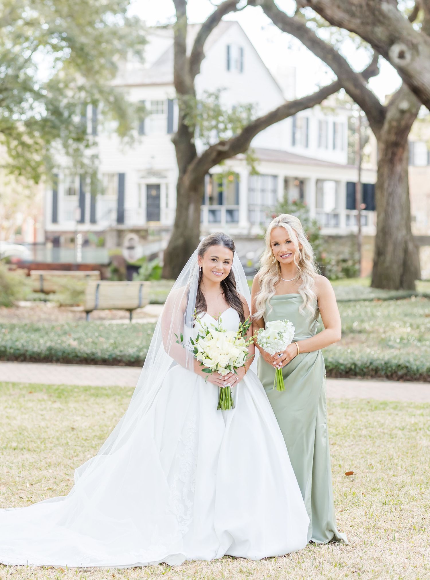 Wedding party poses on lawn with white gowns and sage green bridesmaid dresses.