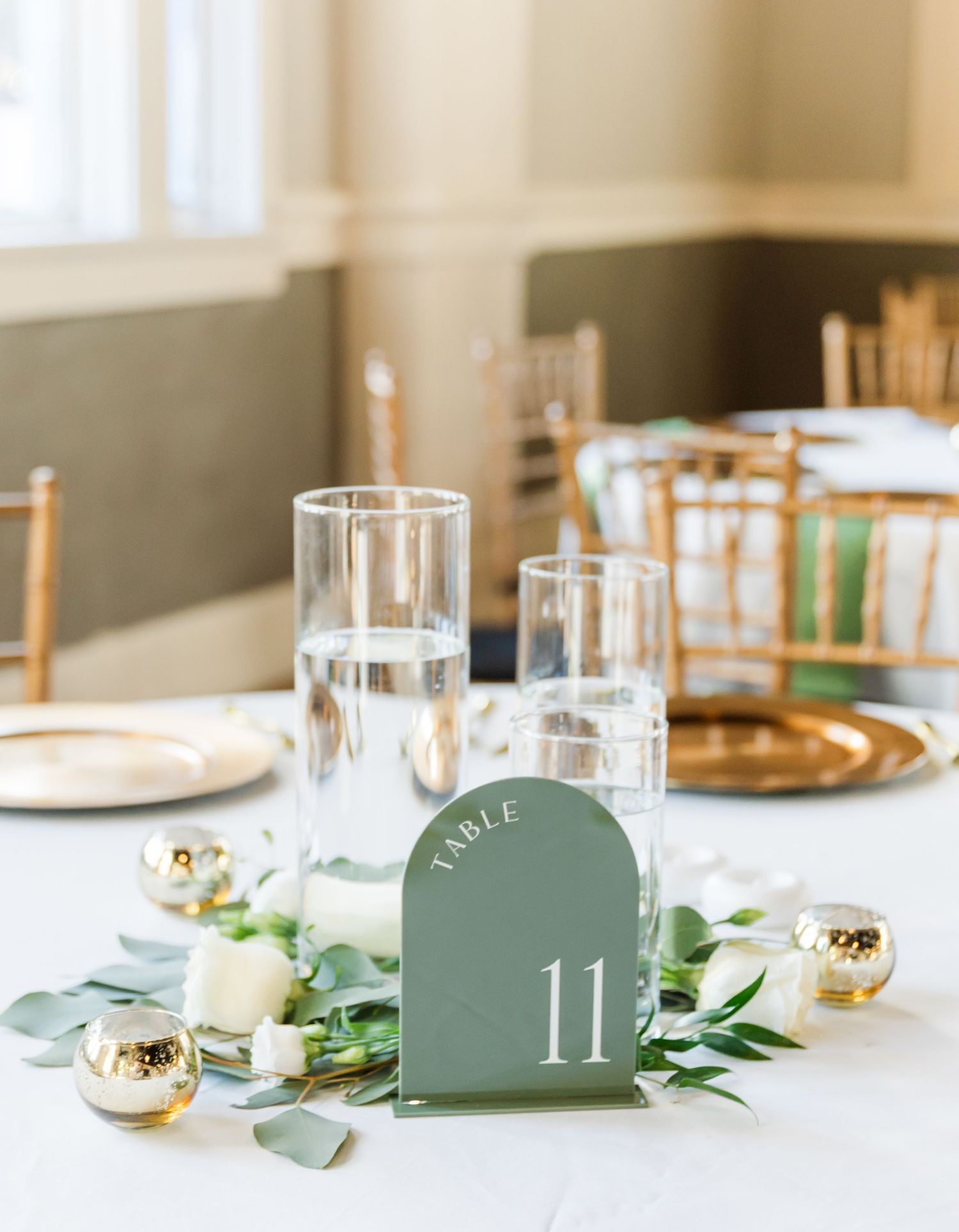Minimalist wedding table setting with sage green table numbers and gold accents.
