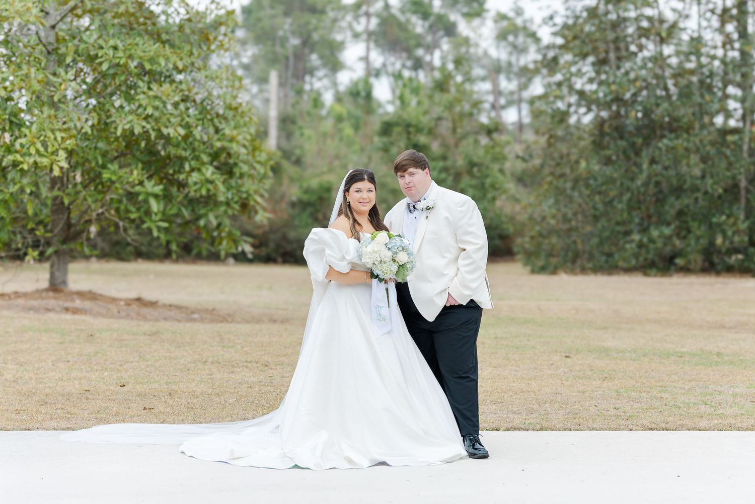 Bride and groom walking together outdoors on wedding day with pine trees in background and long cathedral train.