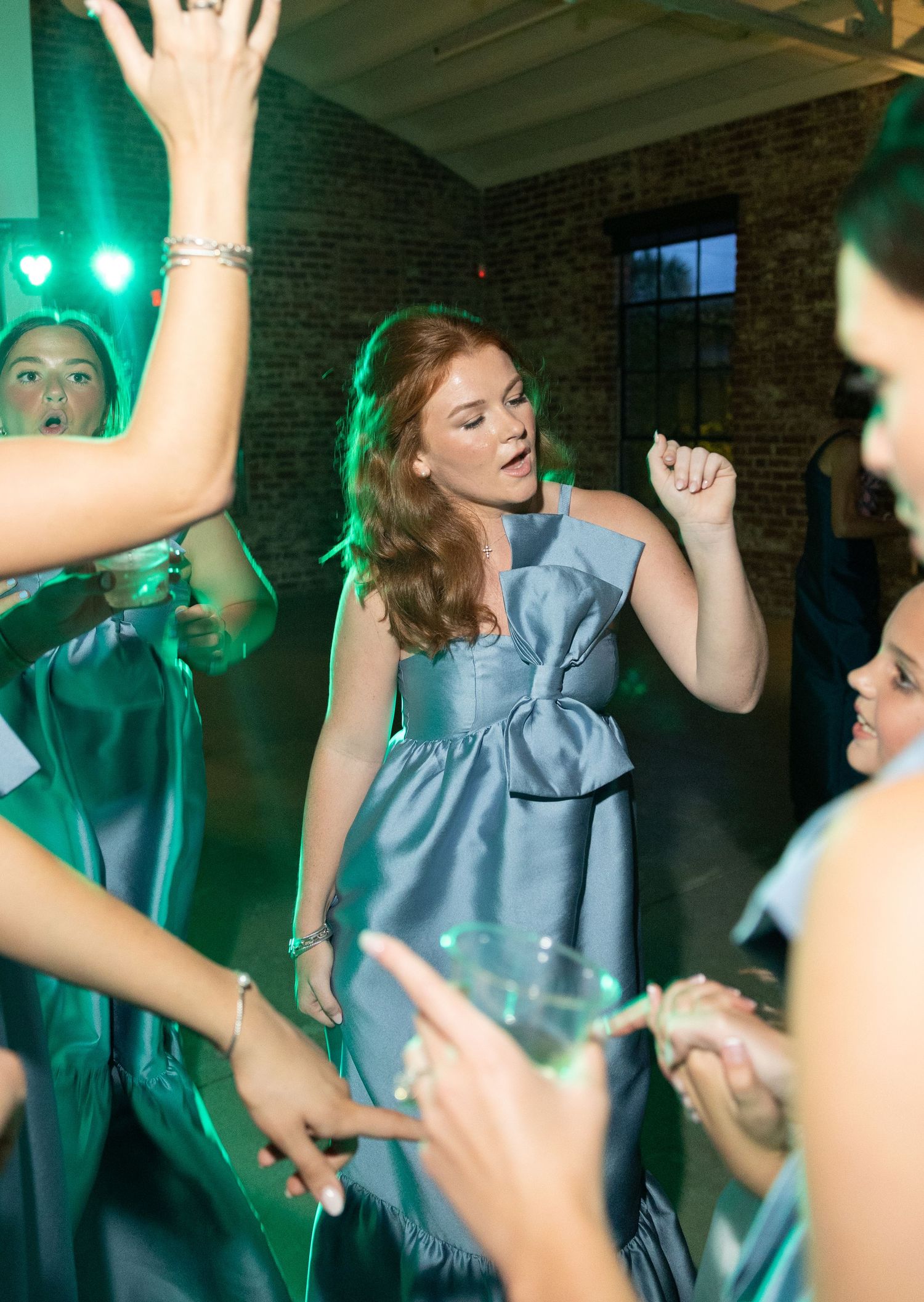 Bridesmaid in blue taffeta dress dancing energetically under green lights at wedding reception celebration.