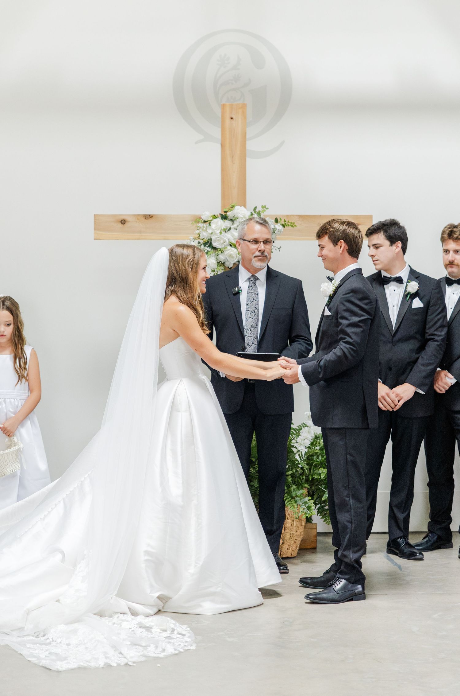 Bride and groom exchange vows before a wooden cross adorned with white florals.
