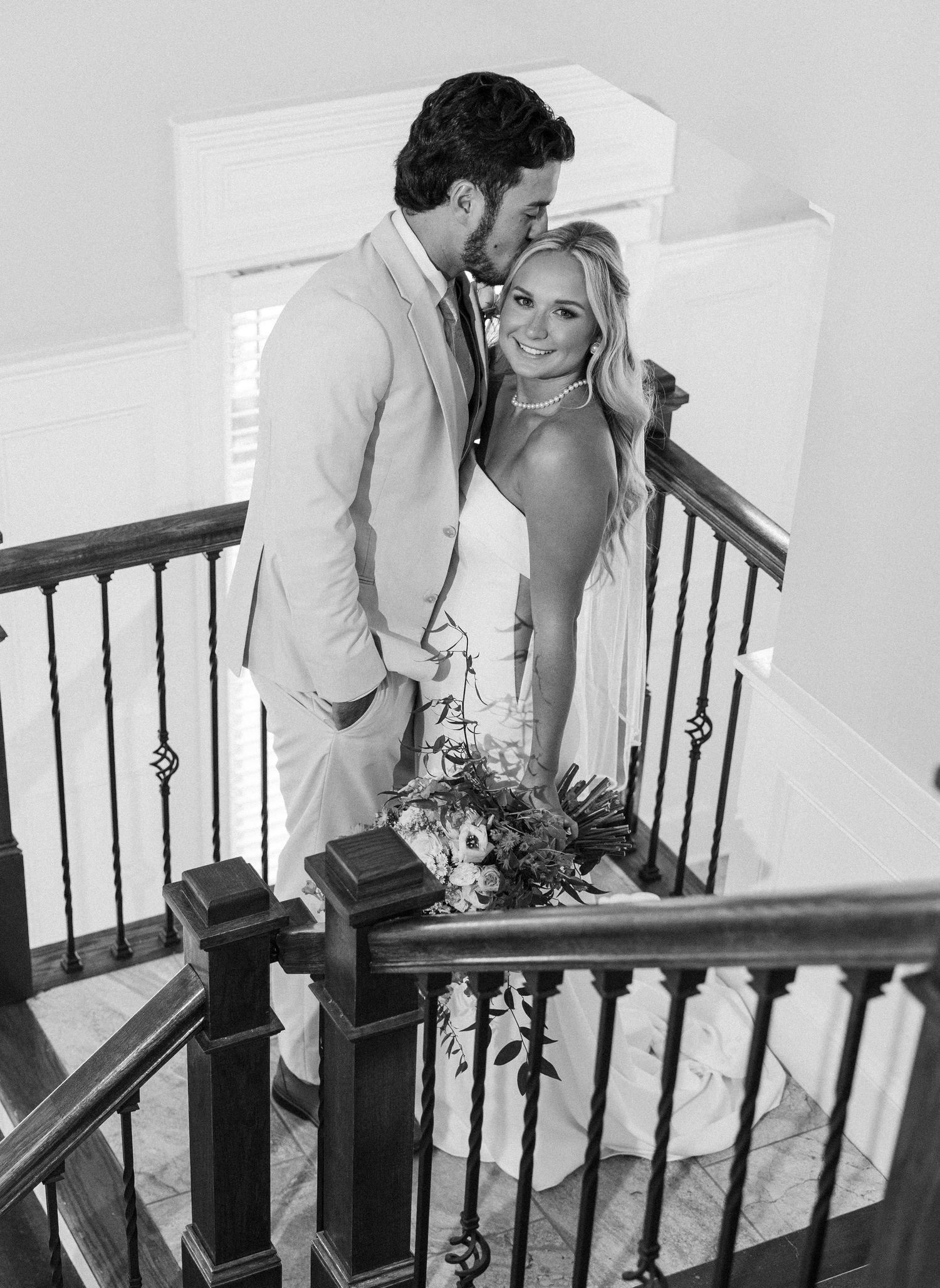 Black and white wedding photo of bride and groom embracing on an elegant staircase.