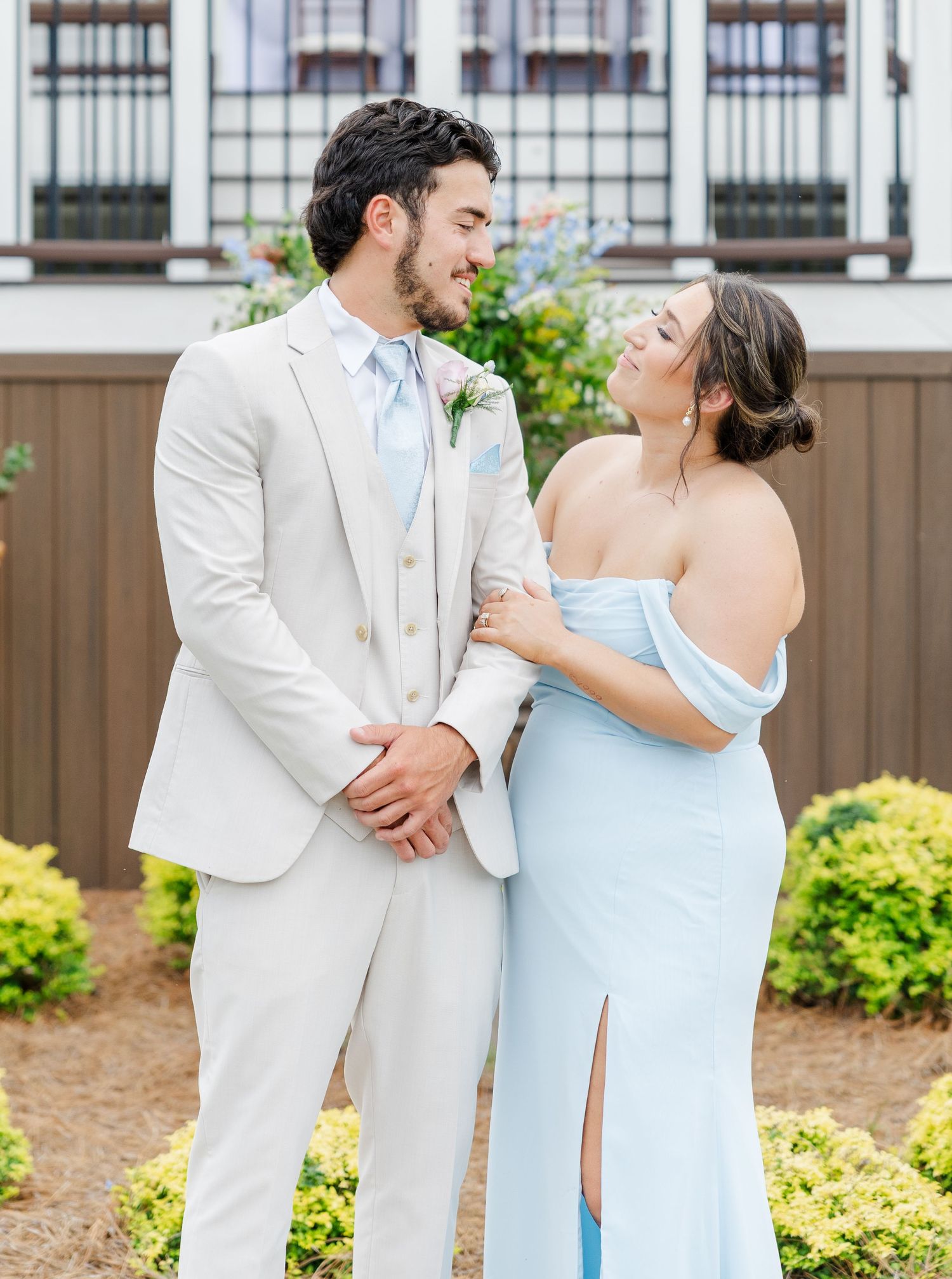 Groom in tan suit with light blue tie smiling with bridesmaid in blue off-shoulder gown.
