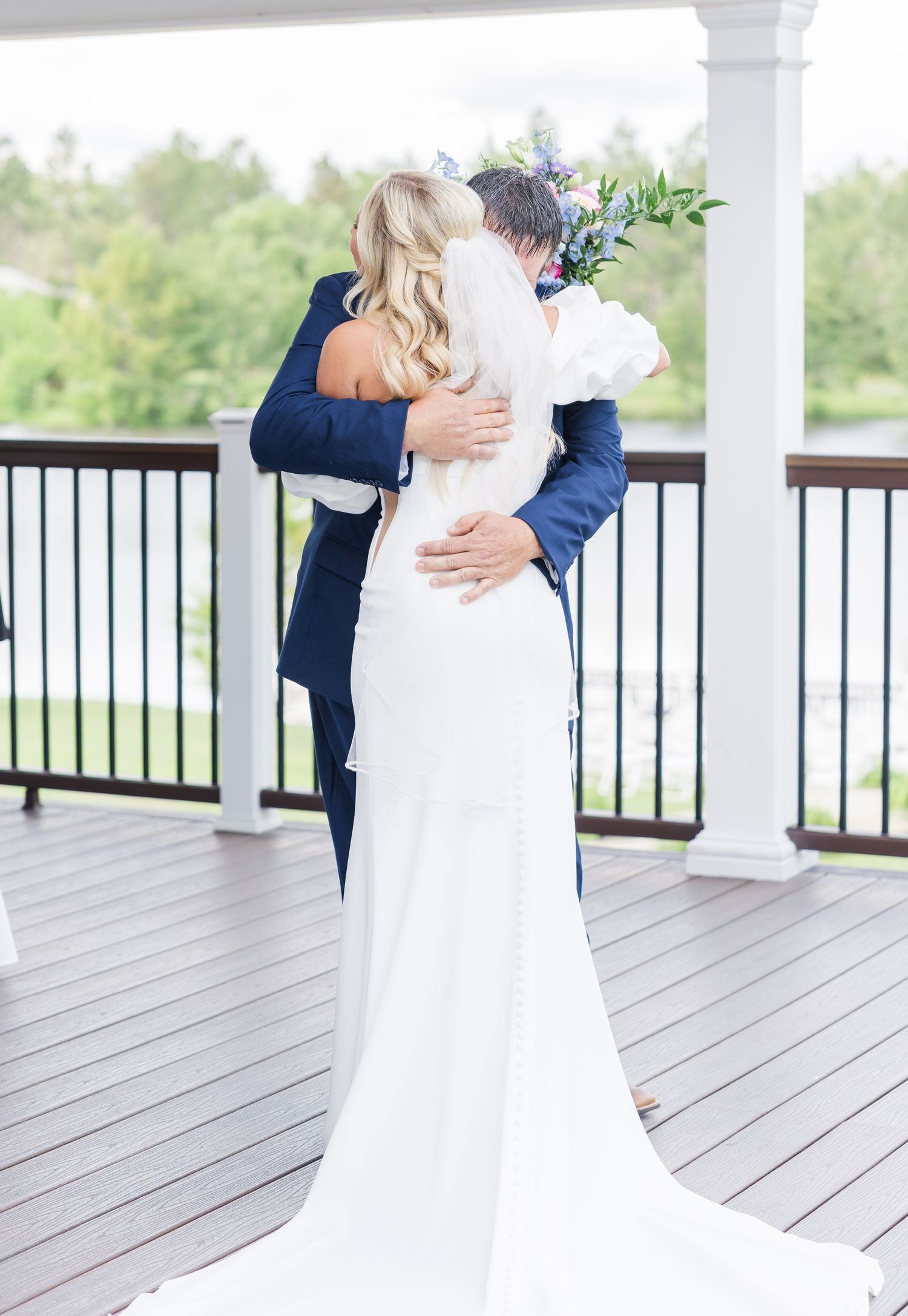 Bride and groom sharing an emotional first look embrace on a wooden deck overlooking a scenic outdoor venue.