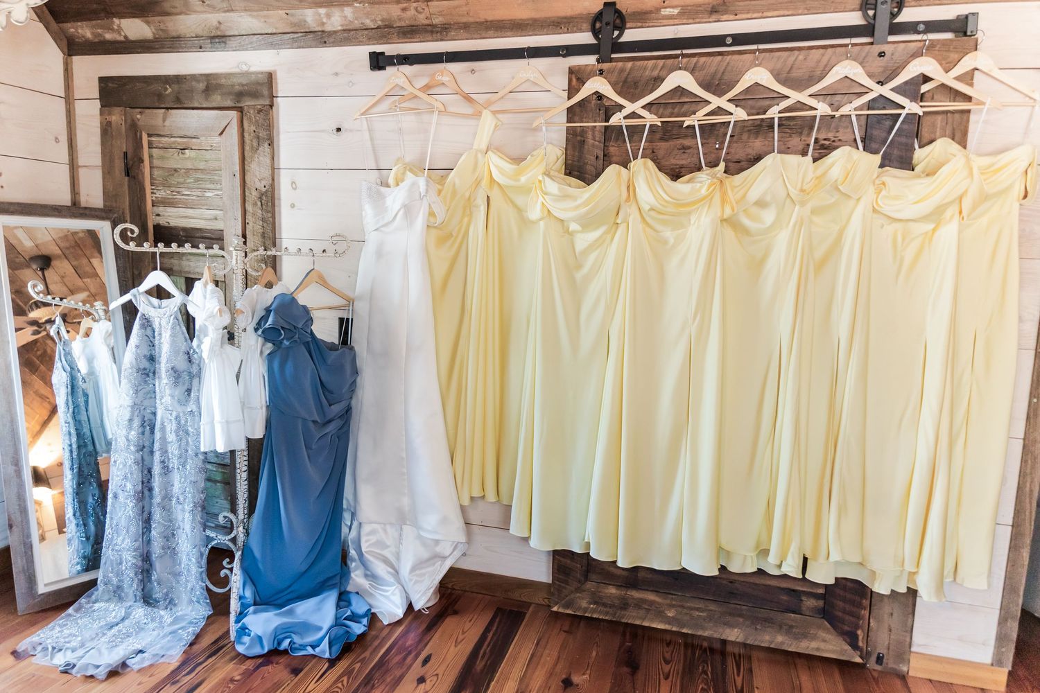 Wedding dresses and yellow bridesmaids gowns hanging on a rustic wooden rack in a barn venue.