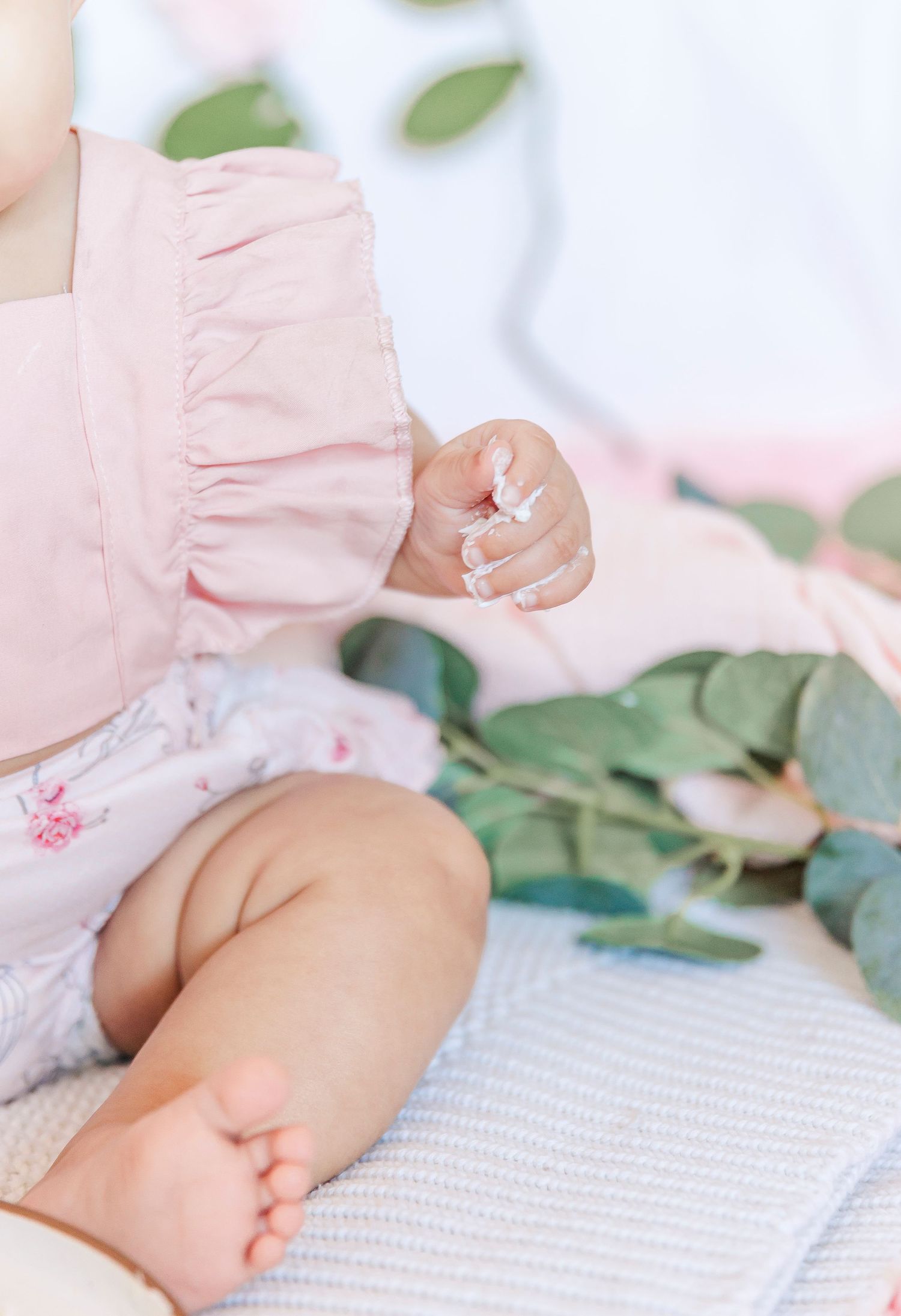 Close-up detail of baby wearing pink ruffled outfit against floral backdrop.
