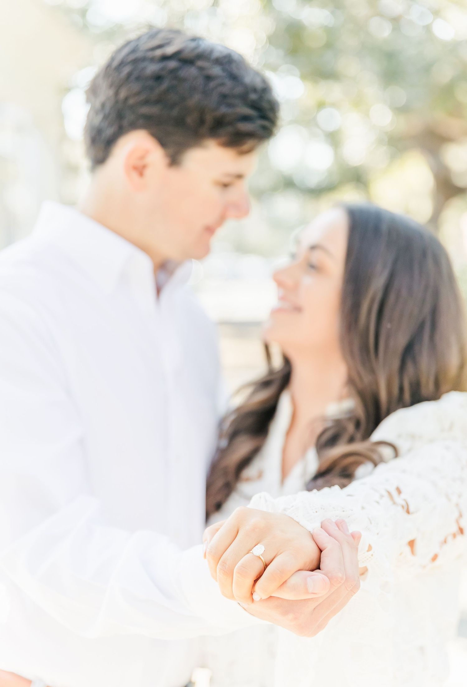Close-up of couple's engagement ring and tender embrace in soft natural lighting.