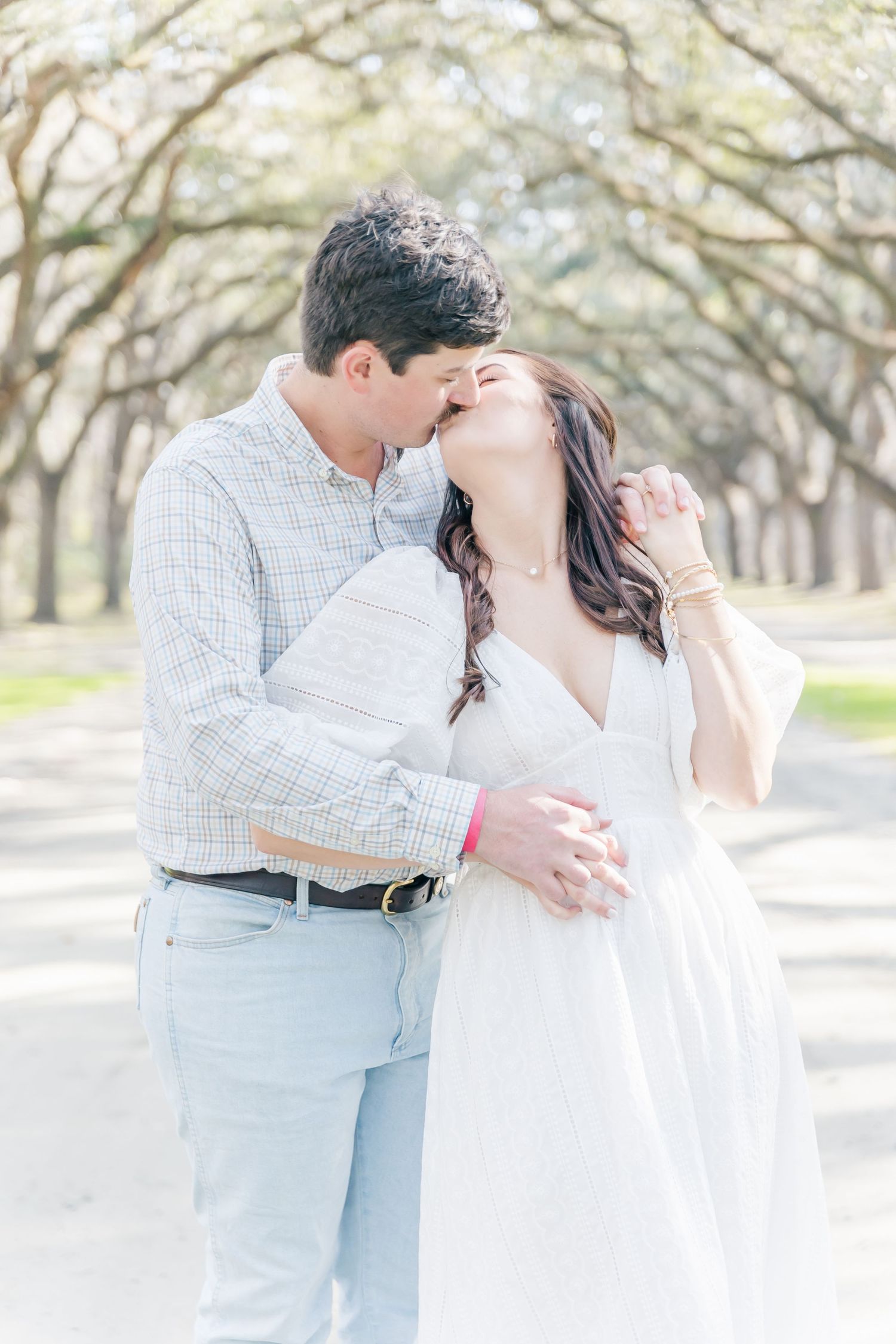 A tender moment captured between a couple on a dreamy tree-lined path in soft lighting.
