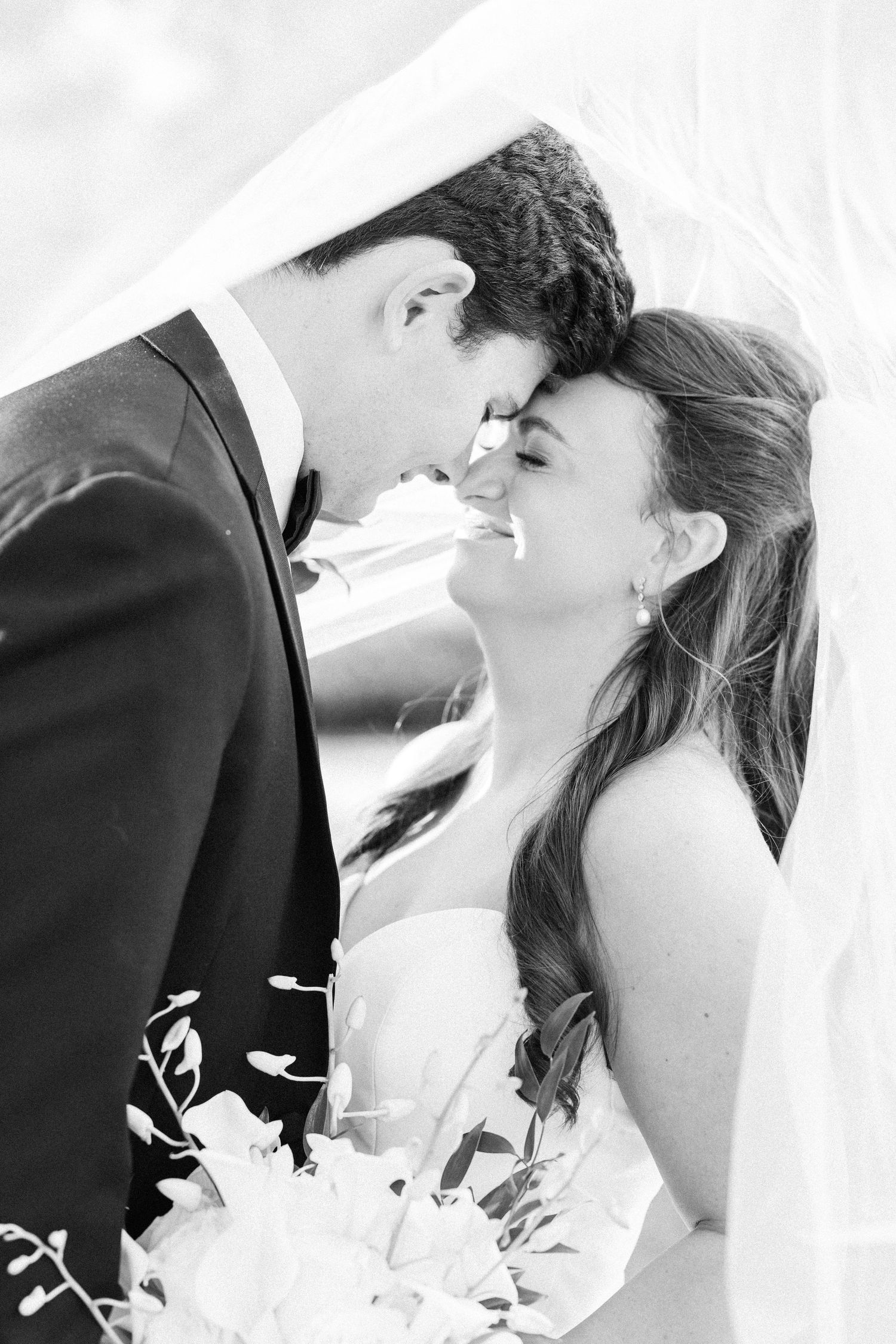 Black and white wedding photo of bride and groom sharing a romantic moment under a veil.