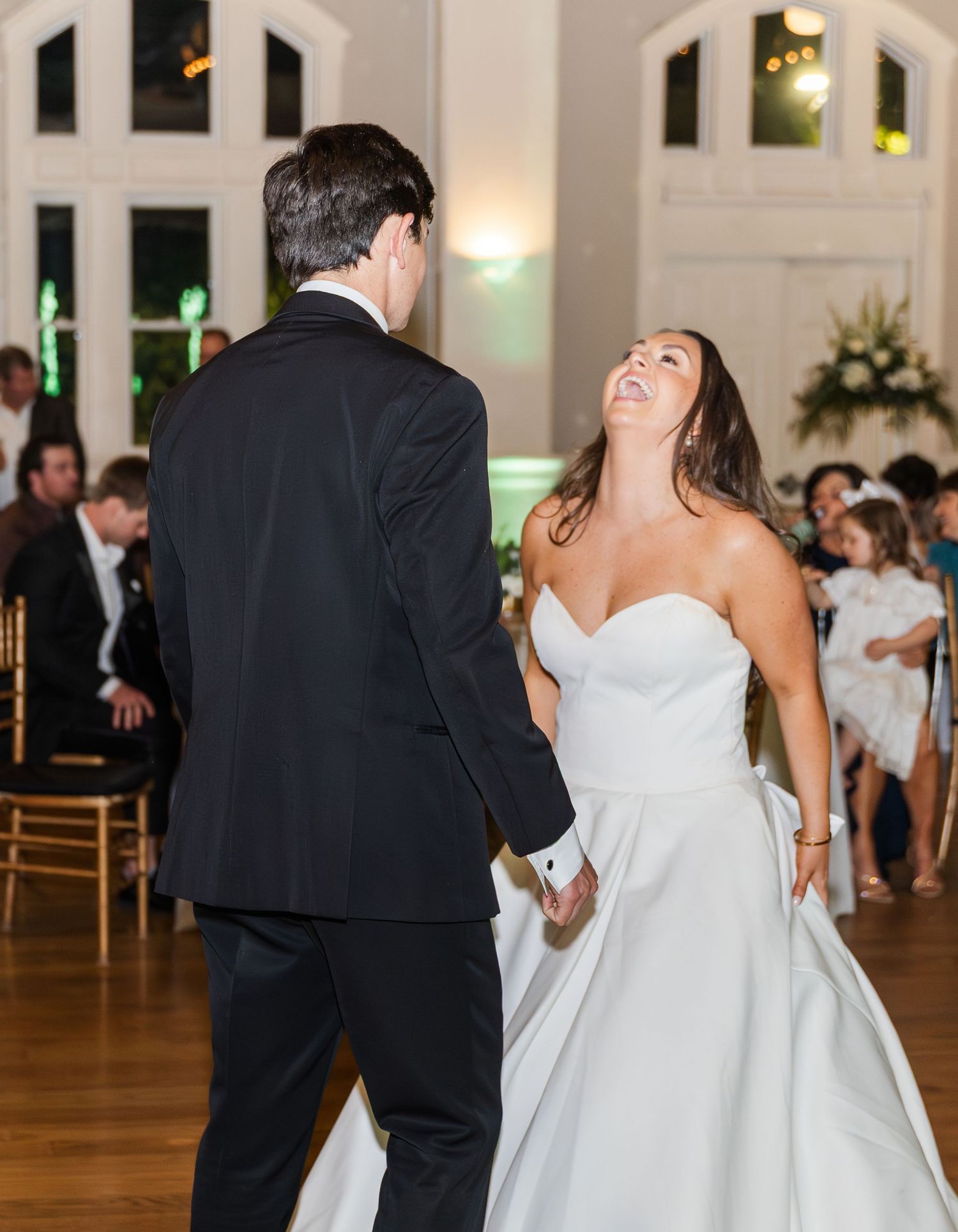 Bride in strapless white gown laughing joyfully with groom during first dance at wedding.