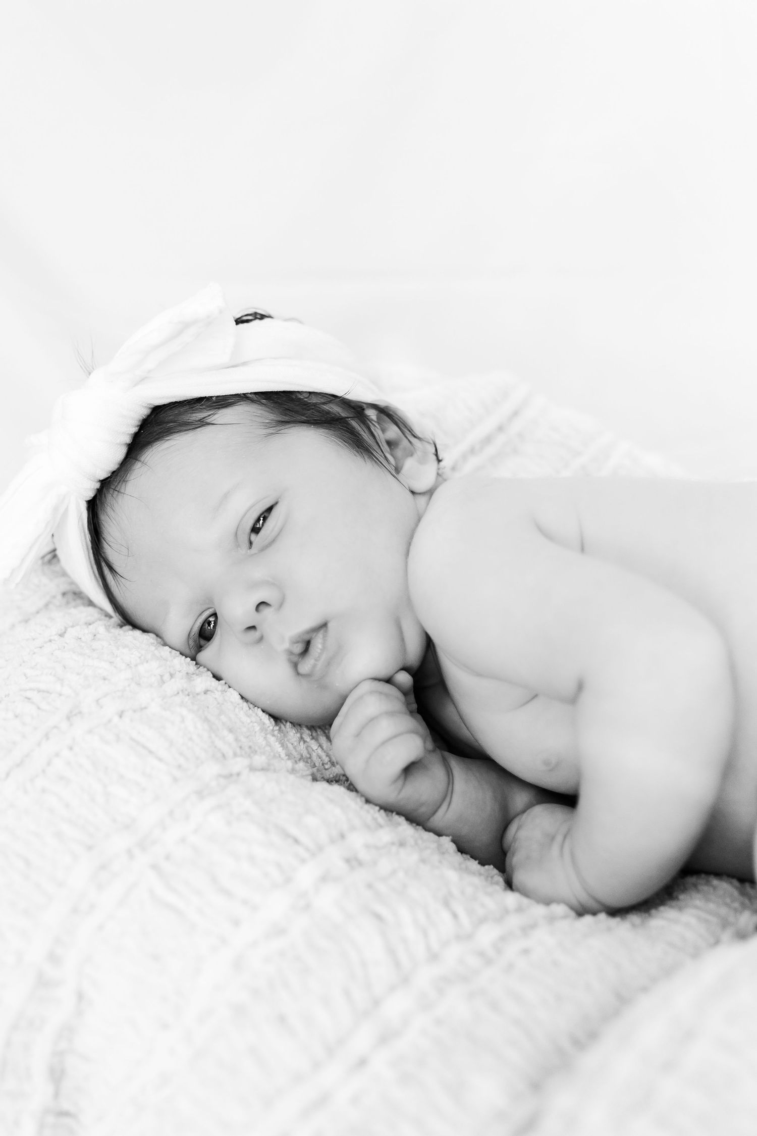 Black and white portrait of a baby resting on textured fabric with a white bow.