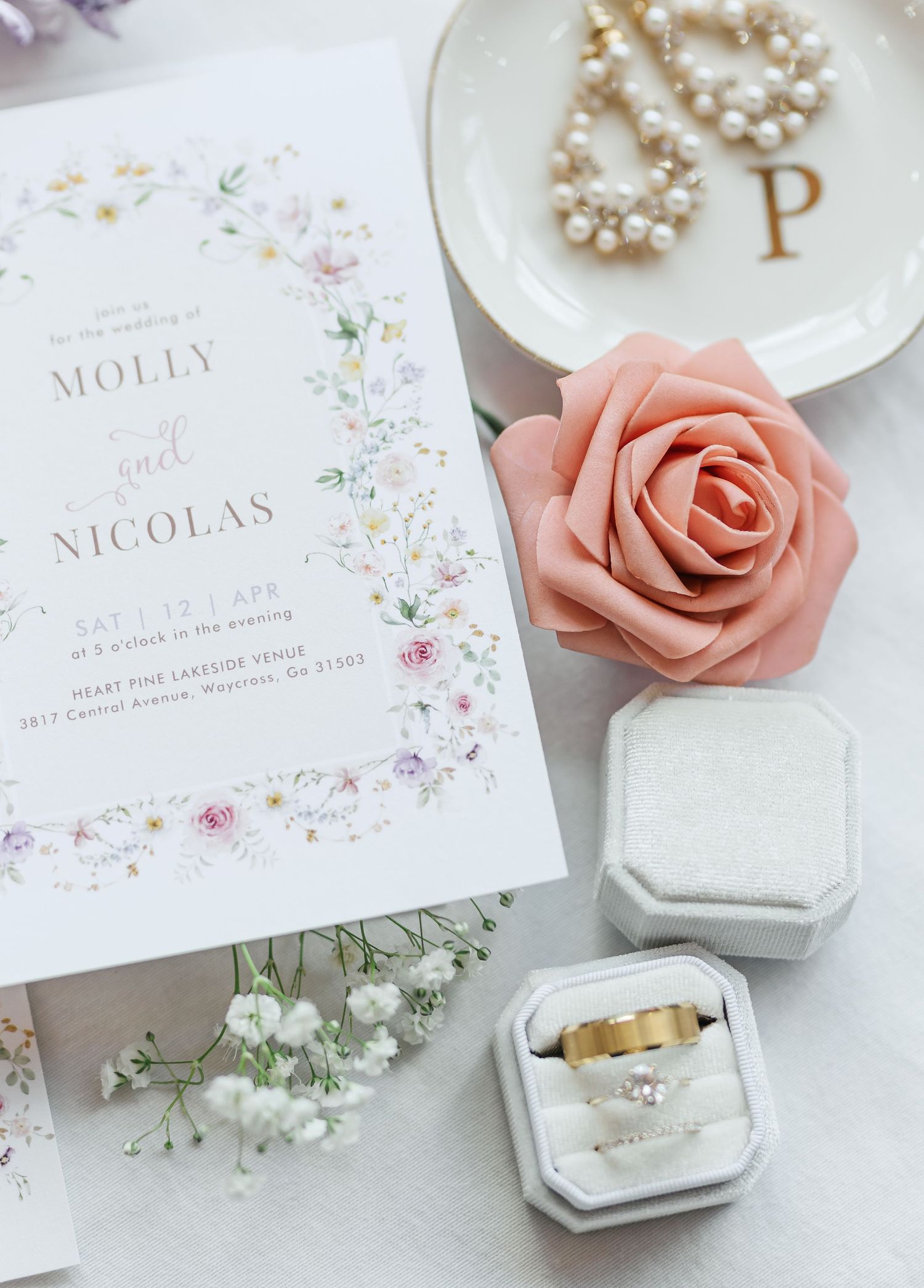 Wedding invitation with floral design, pearl earrings, and pink rose on white background.