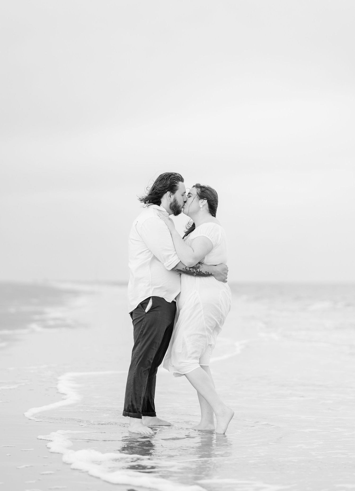 A black and white photo of a couple sharing a romantic moment in the ocean surf.