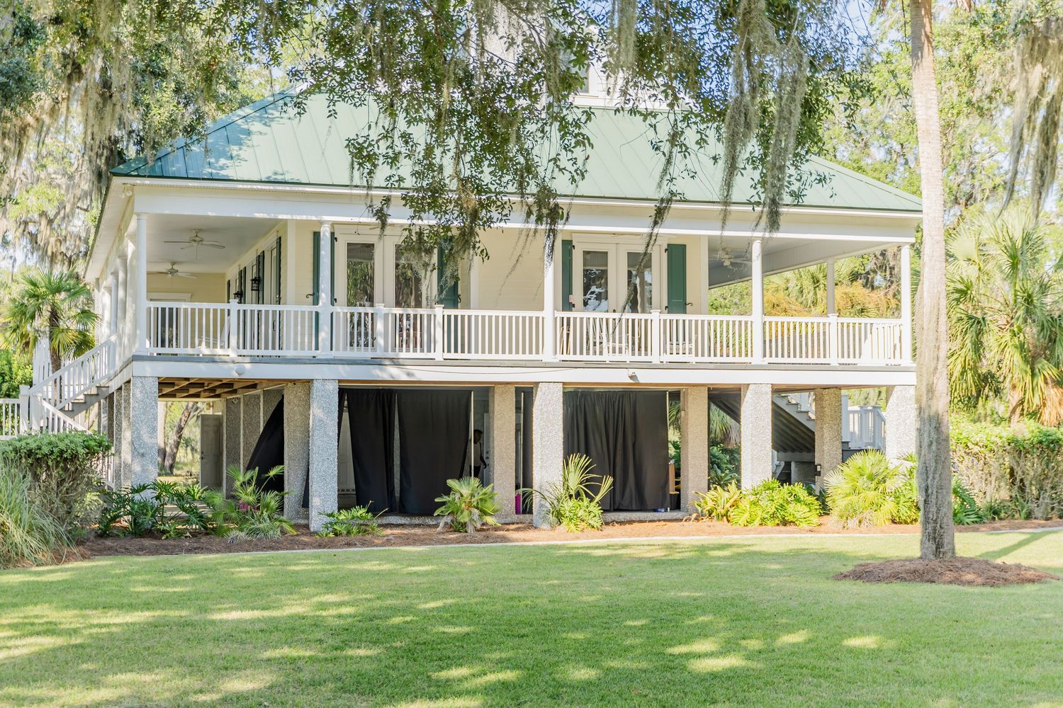 Southern plantation-style house with wraparound porch surrounded by oak trees and Spanish moss.