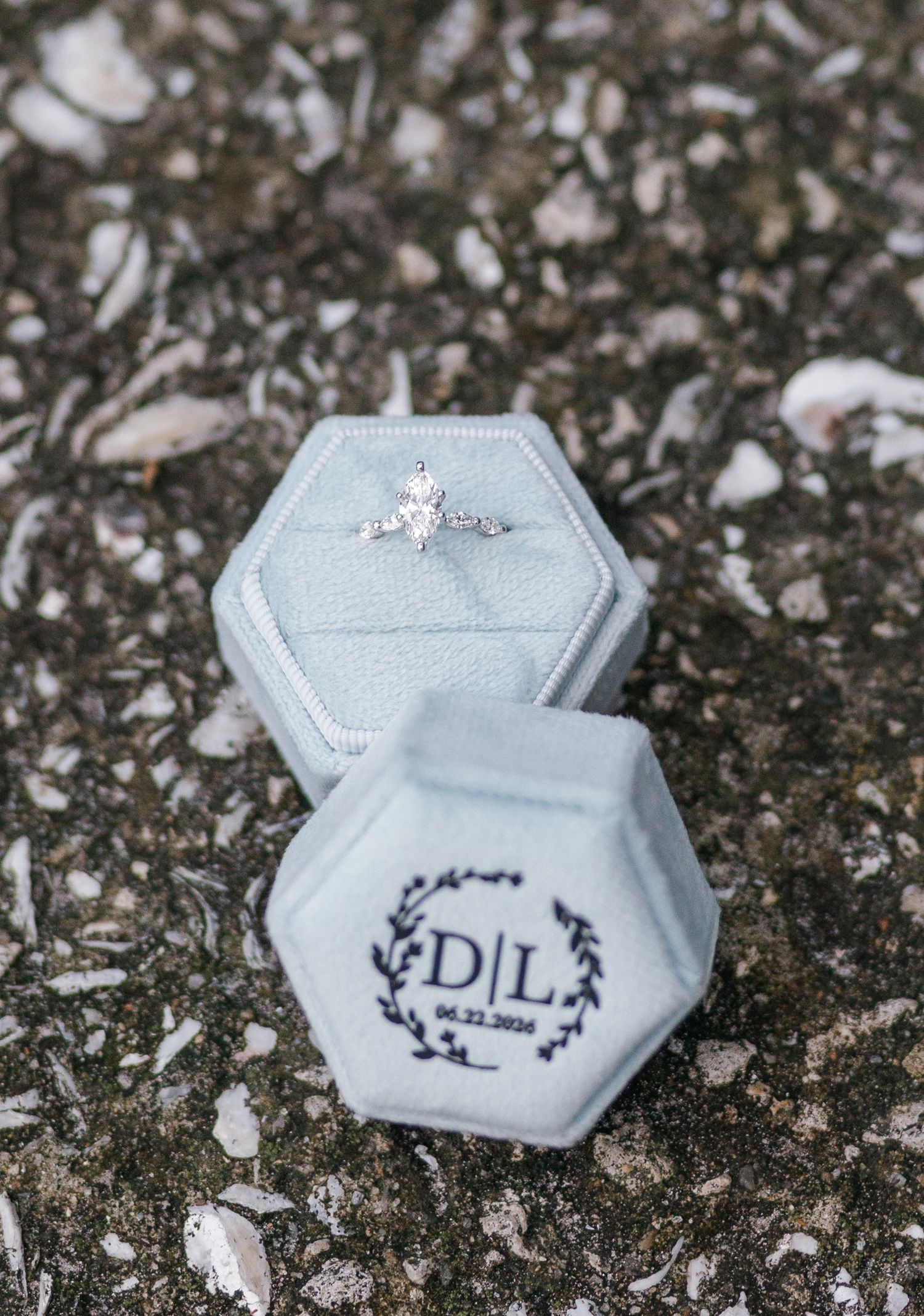 Diamond engagement ring displayed in a personalized gray velvet hexagon ring box monogrammed with D|L and date 04.22.2026.