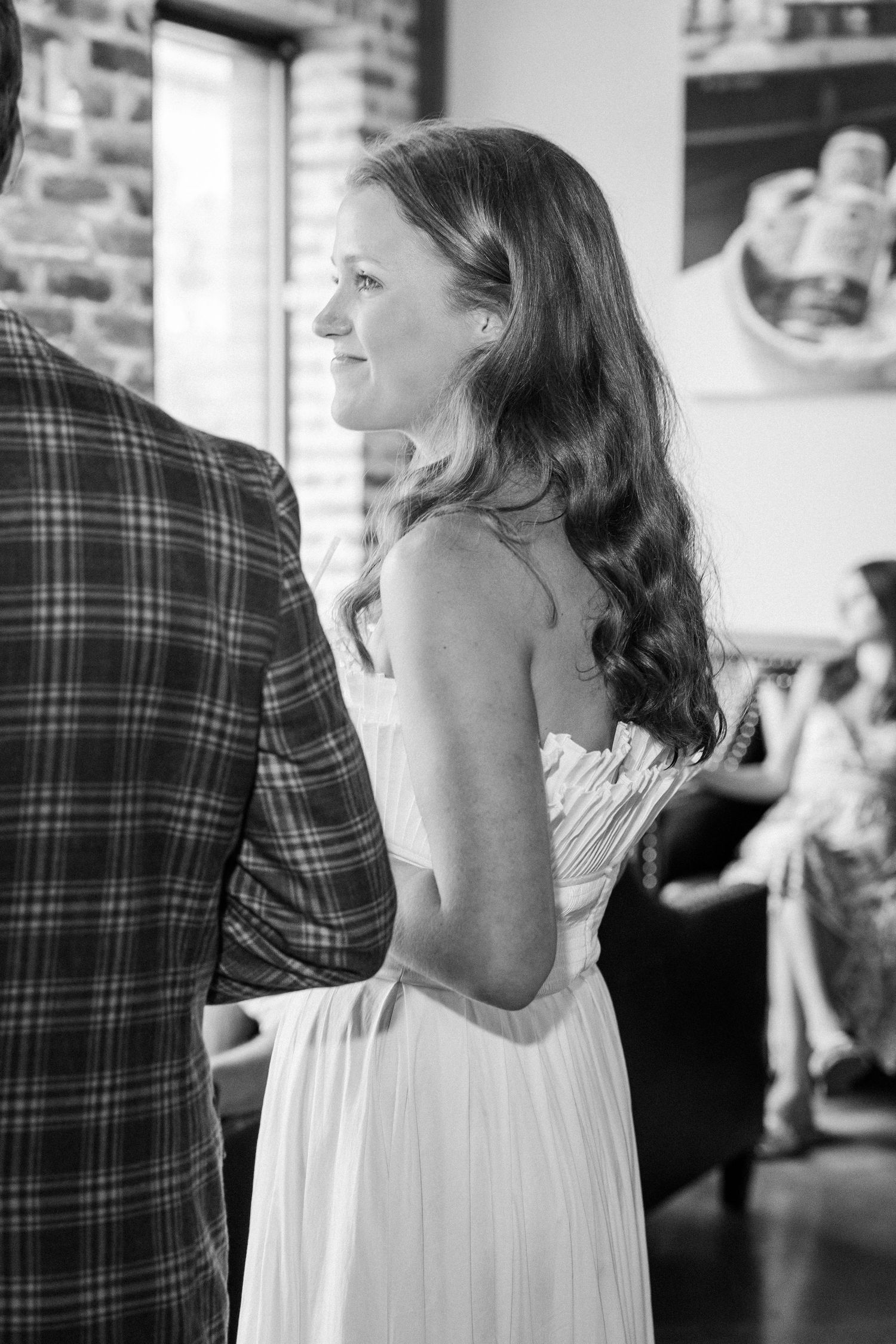 Black and white photo of a bride in a strapless white gown smiling during her wedding ceremony indoors.
