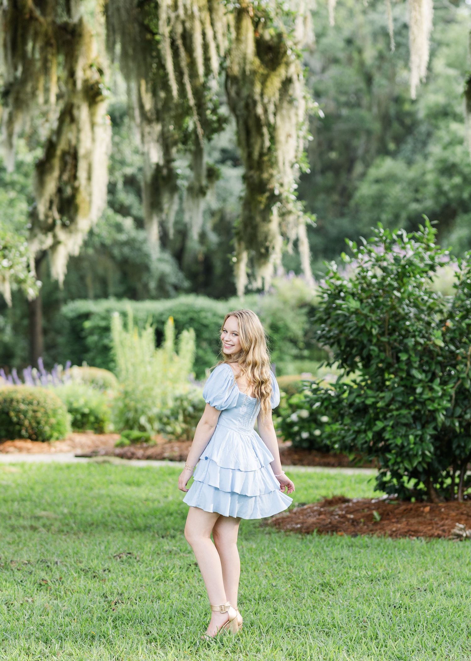 A sequence of photos showing someone twirling in a light blue dress in a green garden with Spanish moss trees.