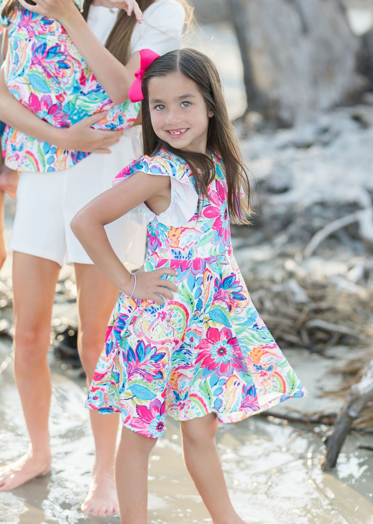 Pink and white floral sundress with ruffled sleeves photographed on a rocky beach setting.