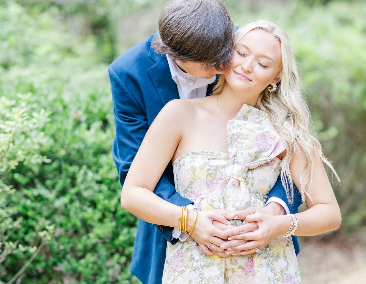 A romantic couple embraces in an outdoor garden setting in a loving and tender moment during a photo shoot.
