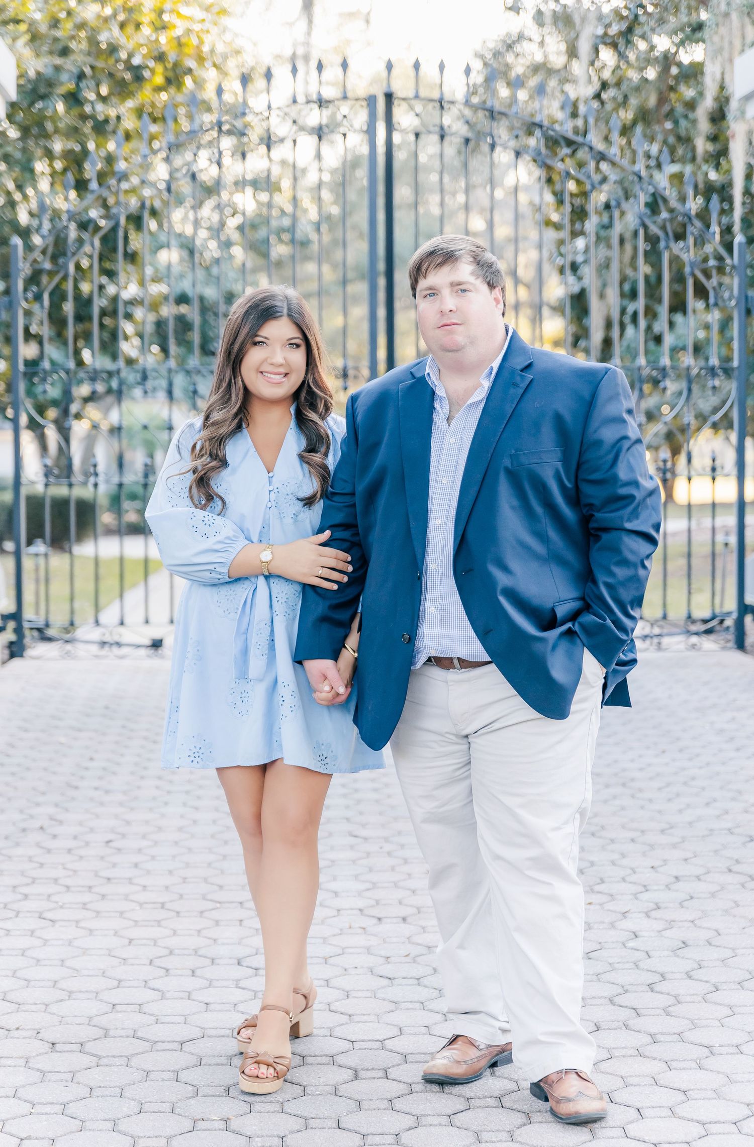 Engagement photo of a couple posing in front of an ornate metal gate in spring afternoon light.