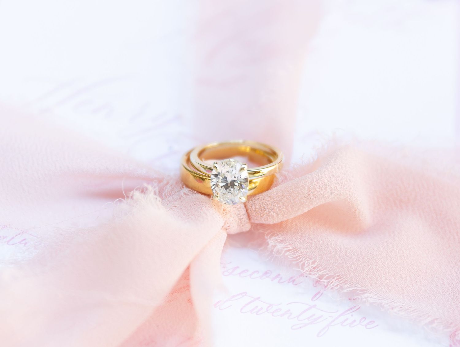 Gold wedding ring with round diamond solitaire nestled in soft pink fabric.