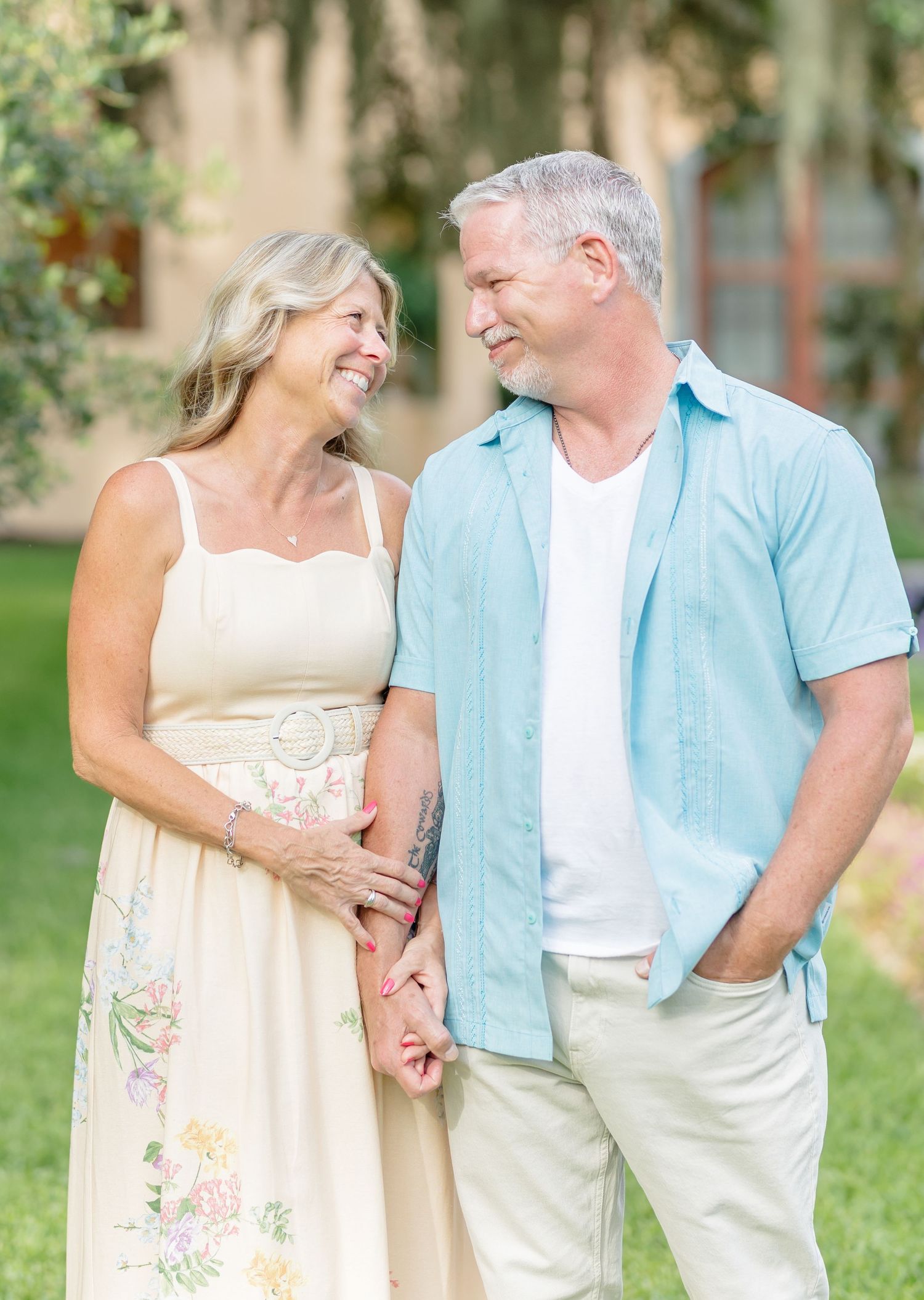 Happy mature couple in coordinated summer outfits sharing candid laughter together outdoors in a garden setting.