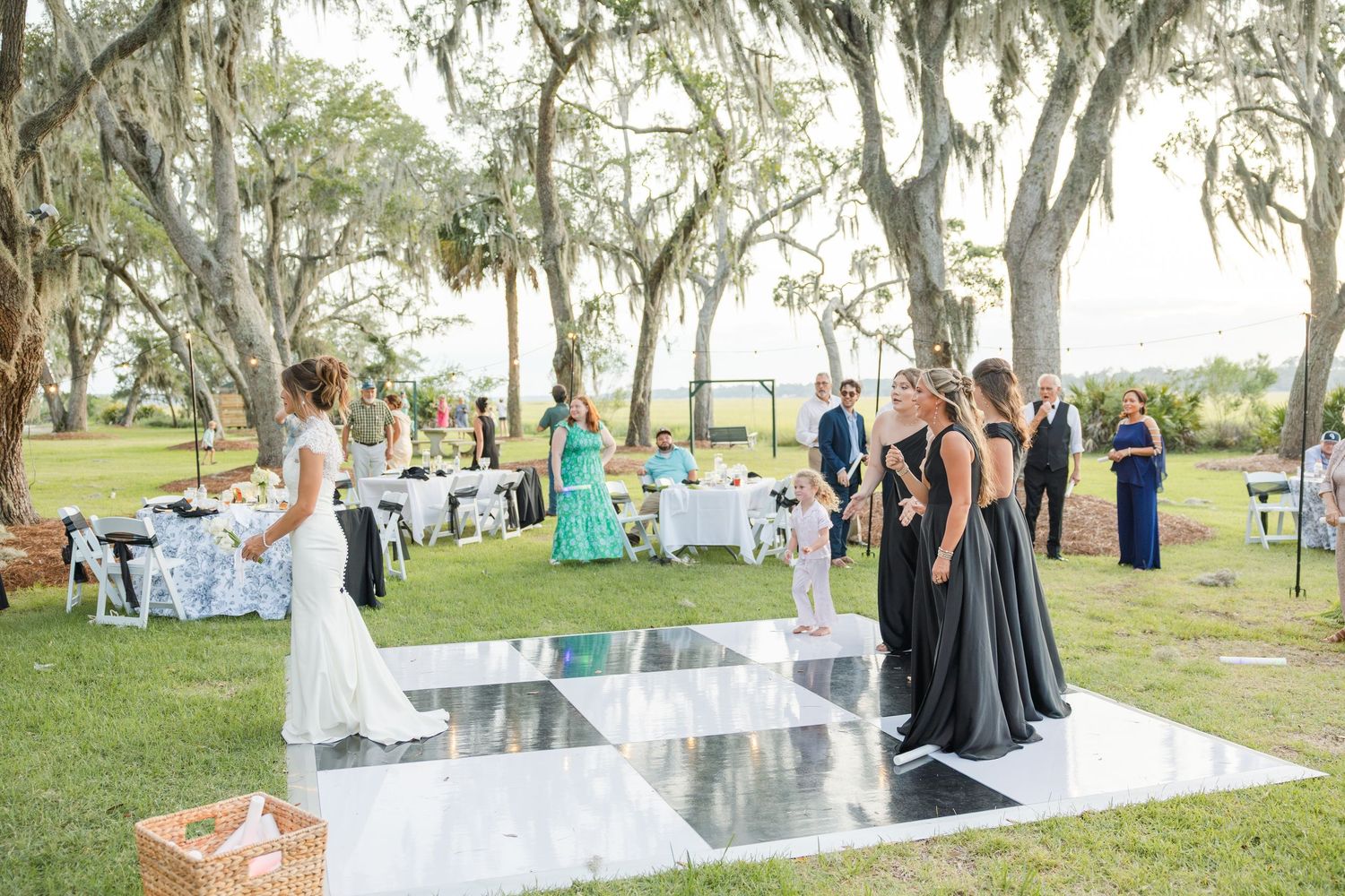 Outdoor wedding reception on mirrored dance floor under Spanish moss oak trees with bridesmaids in black gowns.