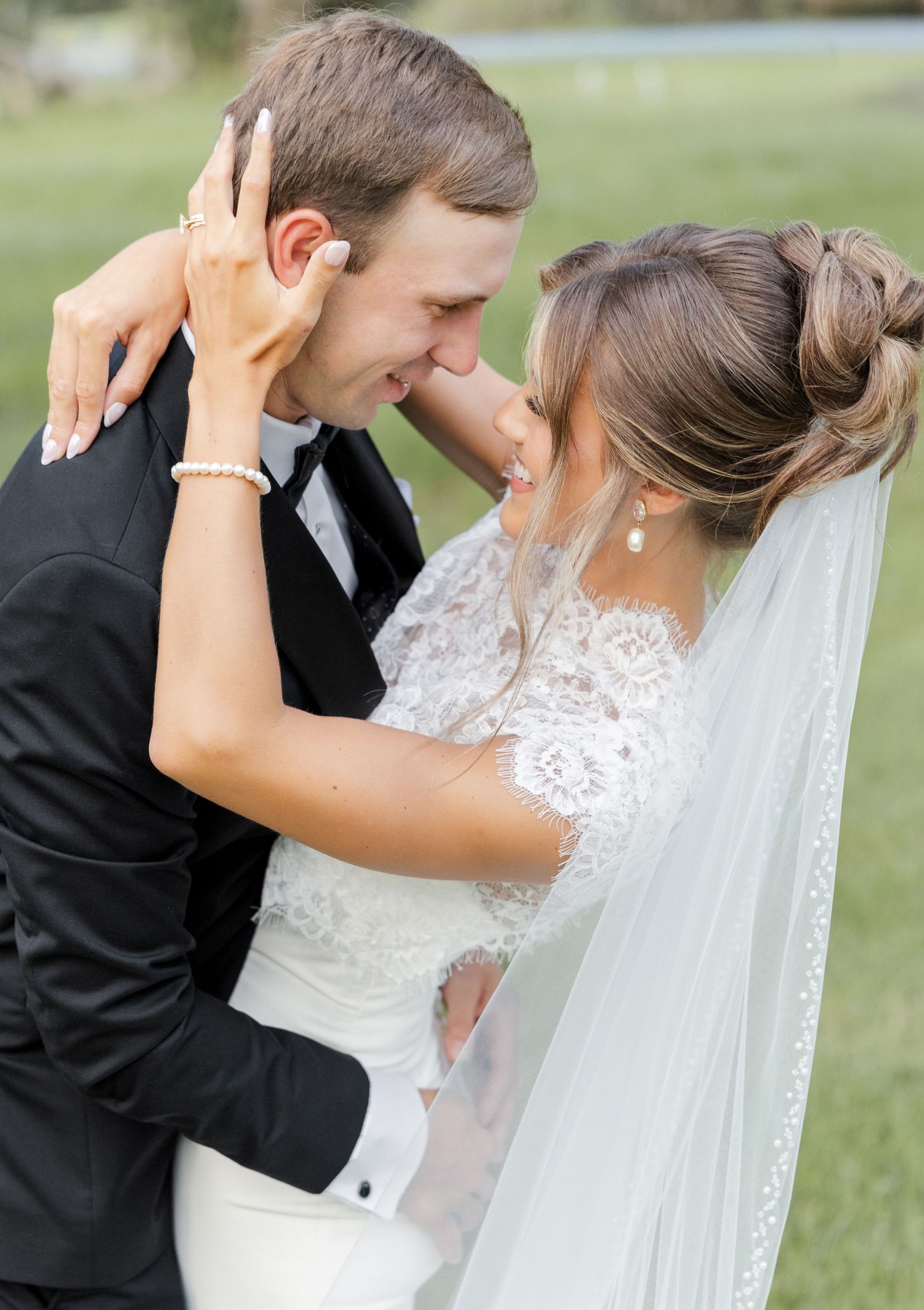 A bride and groom share a romantic moment, nearly kissing, dressed in wedding attire outdoors on their wedding day.