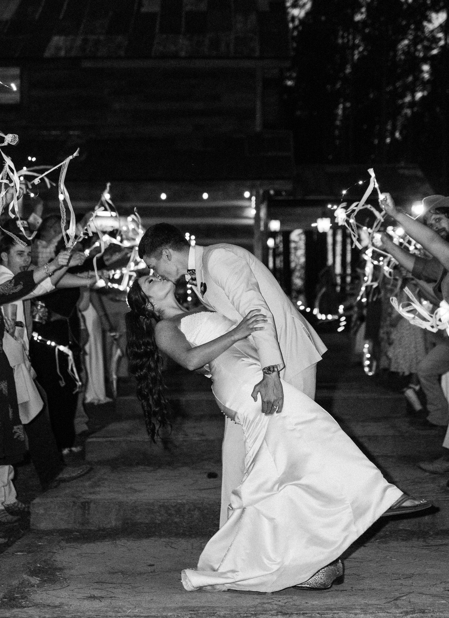 Dramatic black and white photo of groom dipping bride for a kiss during sparkler send-off wedding exit.