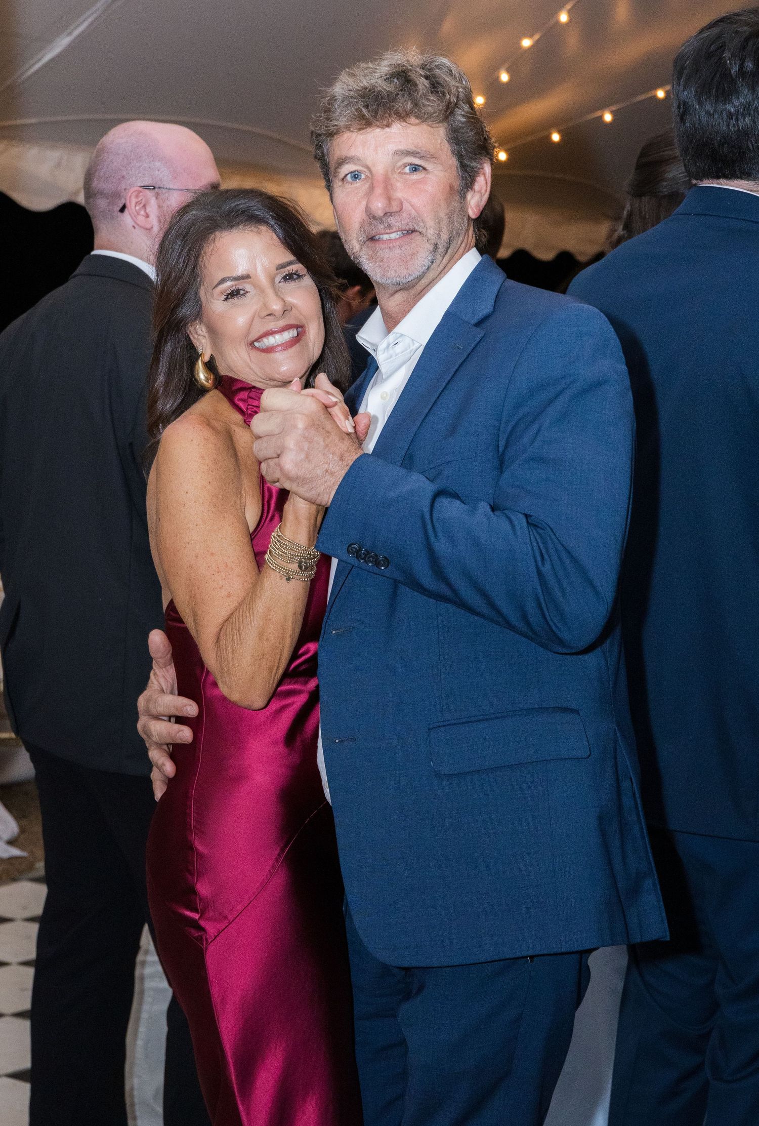 Couple in elegant formalwear share a dance at a wedding reception under a white tent.