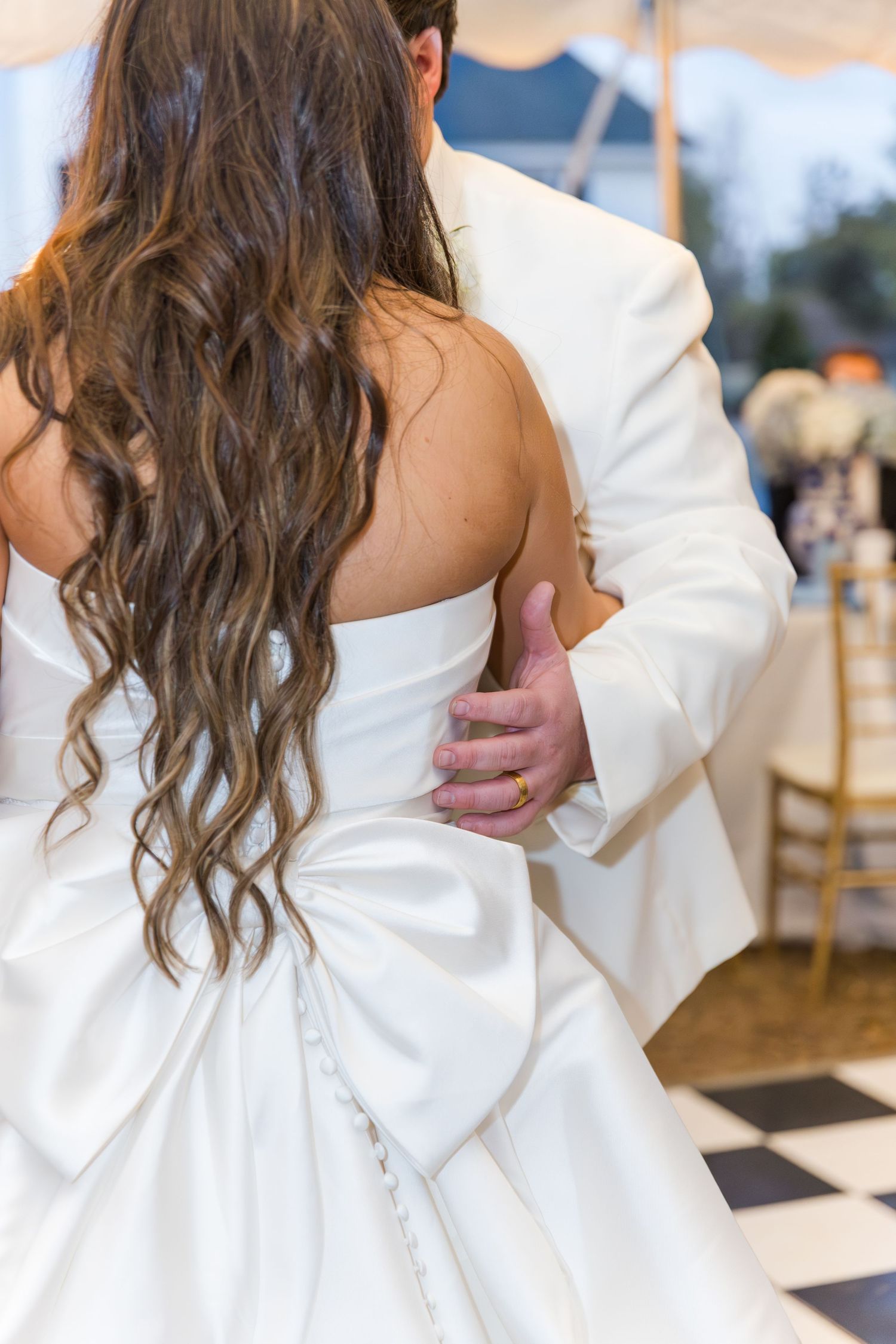 Close-up of bride and groom dancing, showing her long curly hair and white gown with bow detail.
