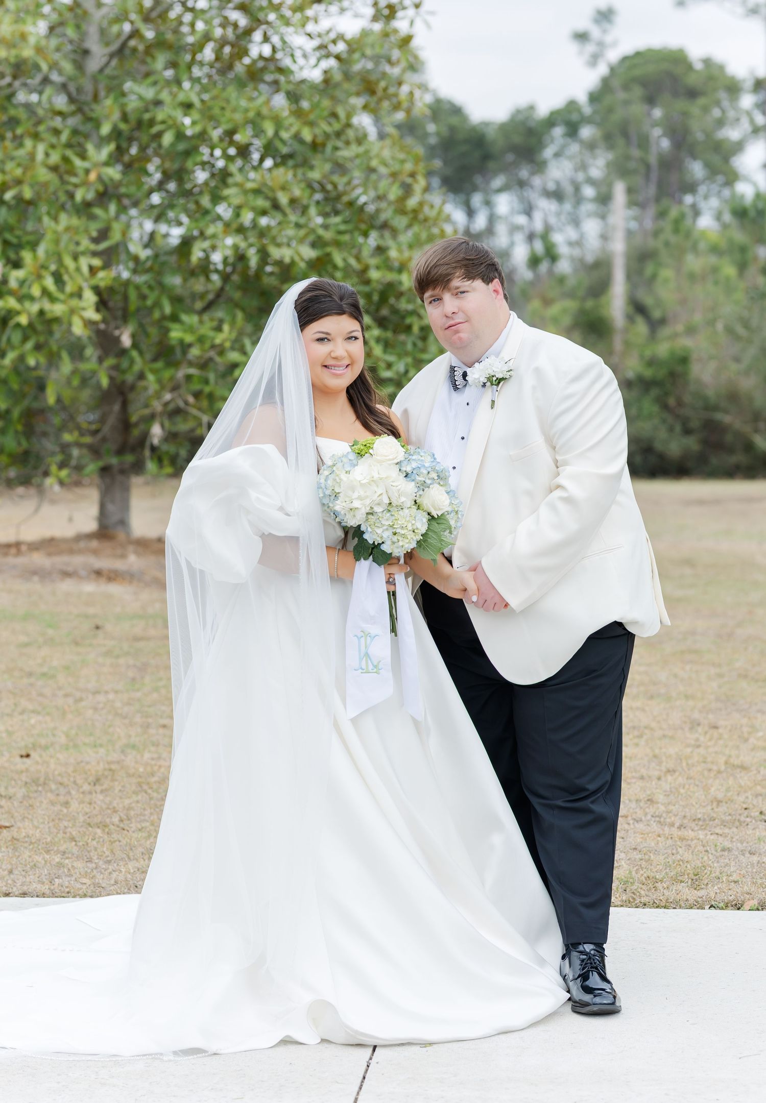 Bride and groom portrait outdoors, bride in white gown with veil holding hydrangea bouquet.