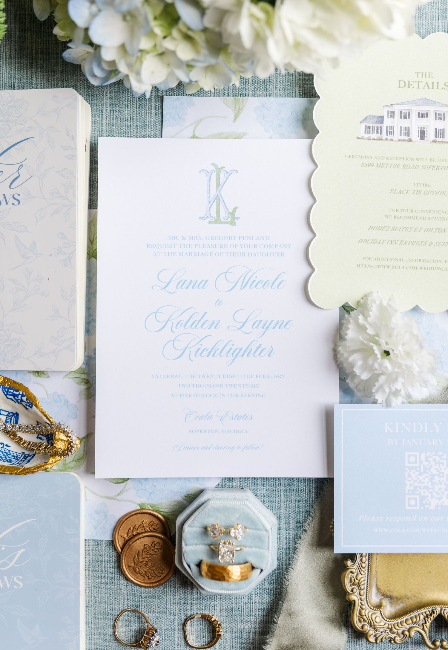 Elegant wedding invitation suite with monogram, rings, and gold wax seals on blue linen background.