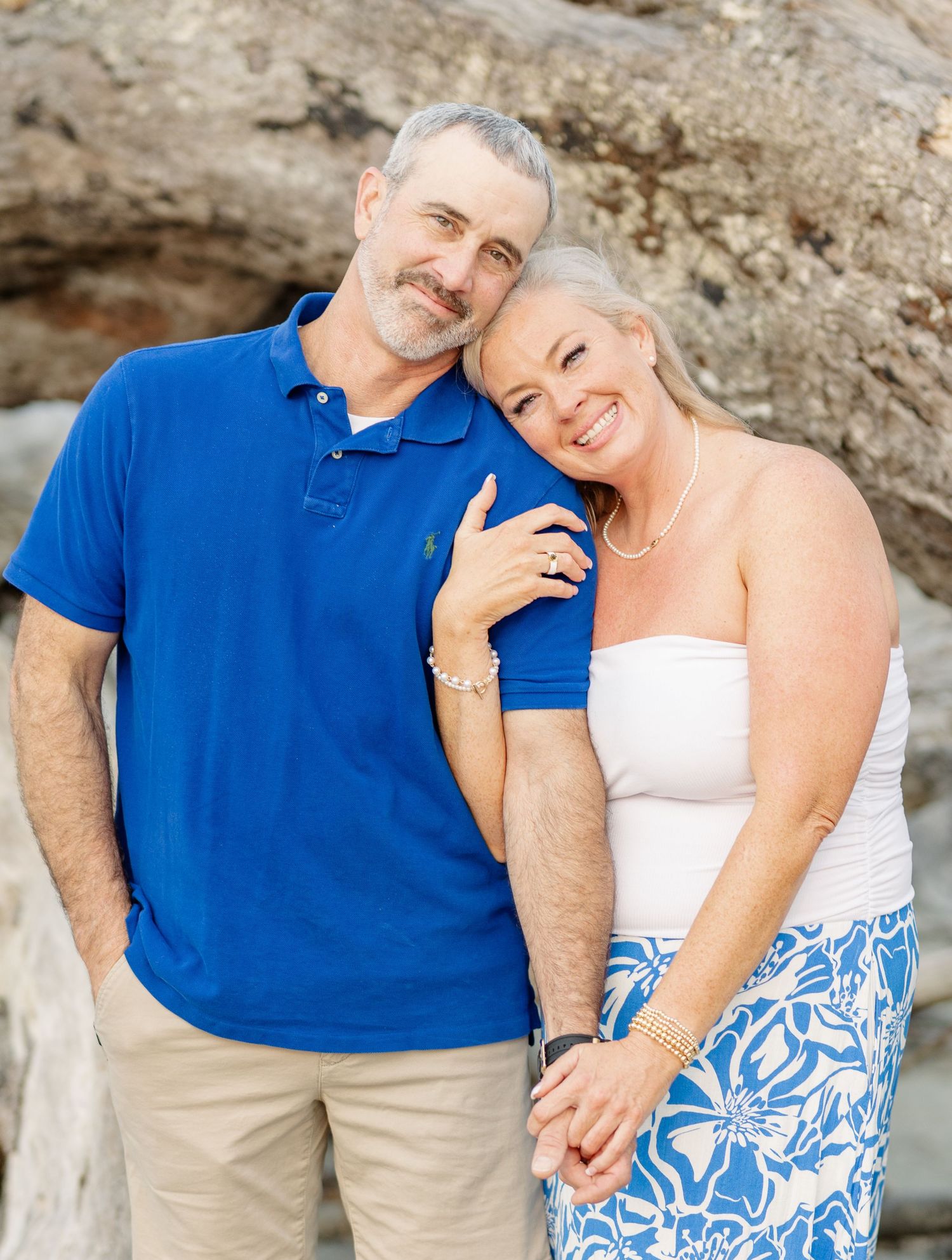 Happy couple in casual attire poses together against rocky backdrop during outdoor photo session.