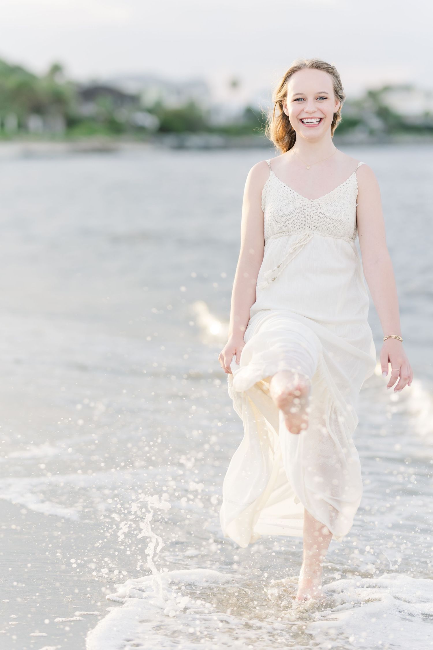 A breezy white dress catches movement while splashing through shallow coastal waters at sunset.