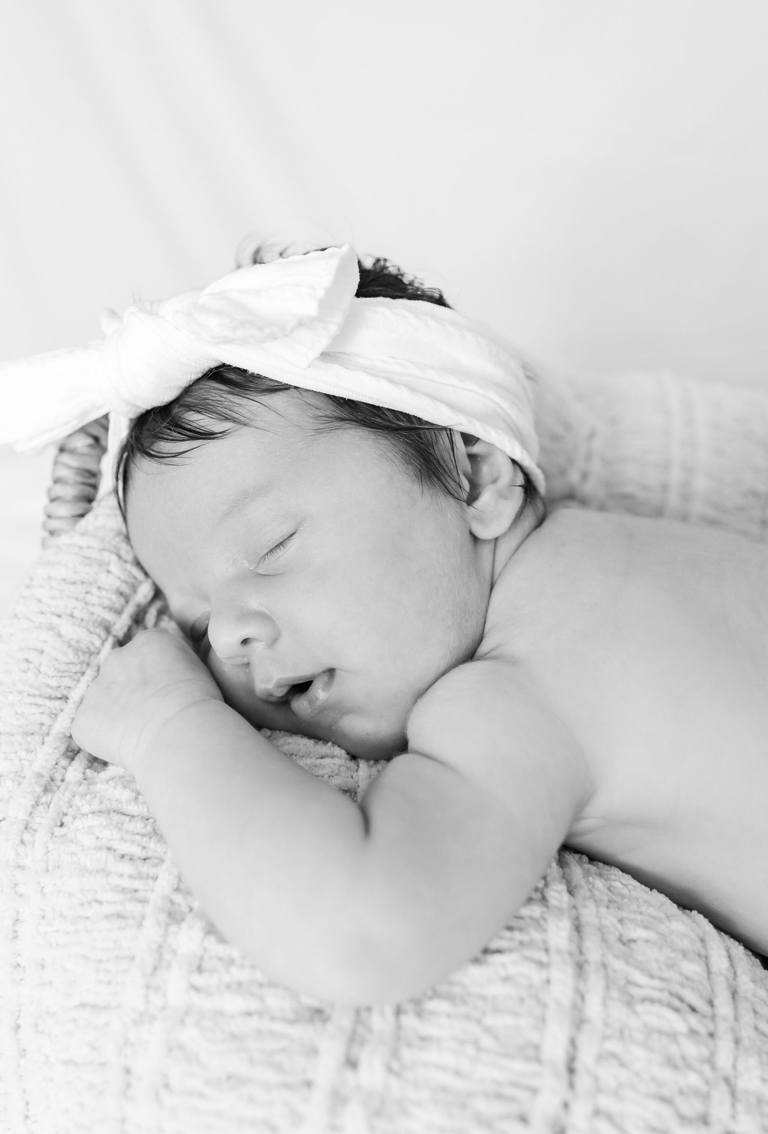 Sleeping baby with white headband rests peacefully on light textured fabric.