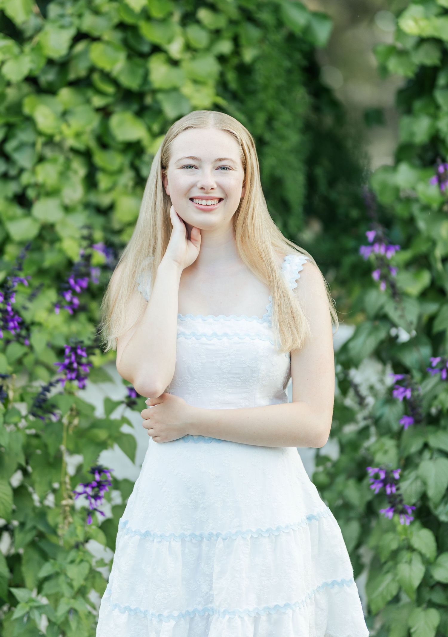 A summer portrait in a garden with purple flowers and greenery in the background.