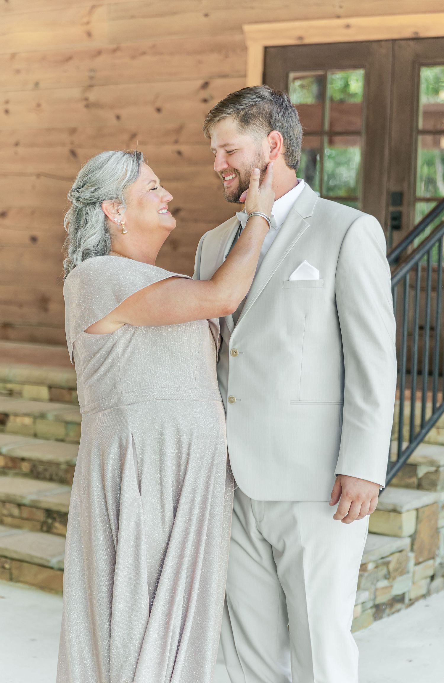 A touching moment between two people in light colored formal wear standing on a wooden porch.