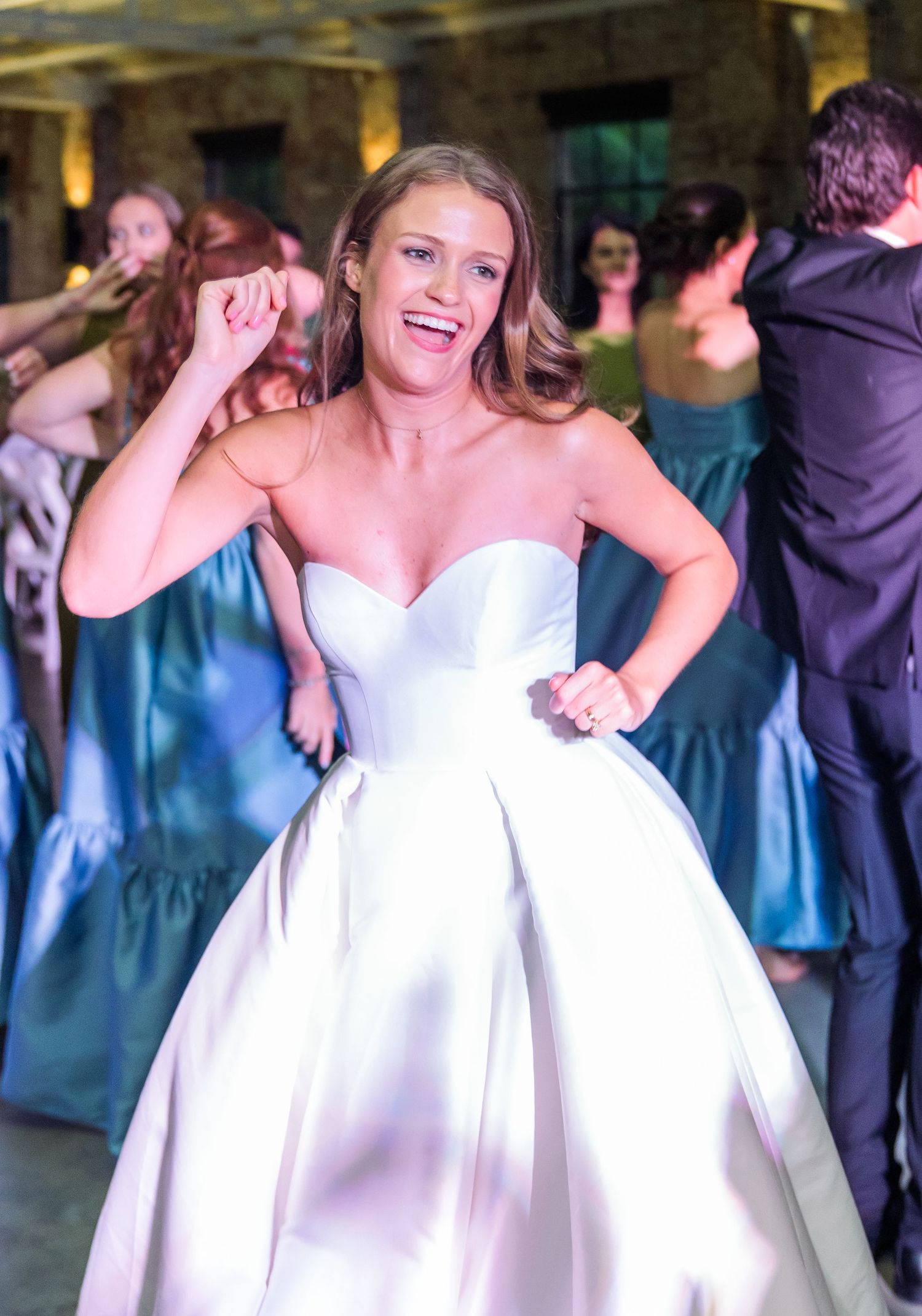 Joyful bride in strapless white satin ballgown dancing energetically at wedding reception celebration.