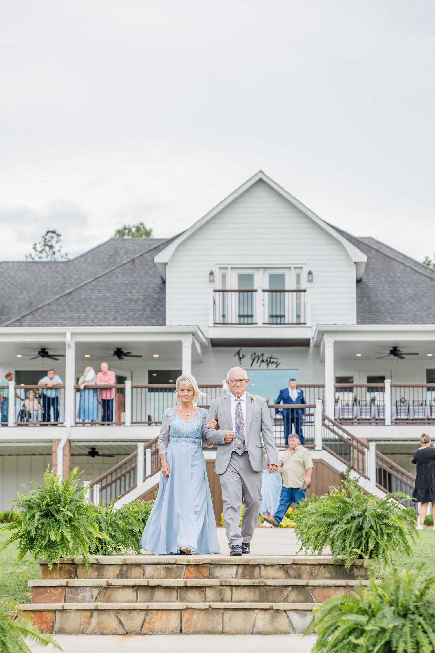 An elegant couple descends stone steps at a white farmhouse wedding venue.