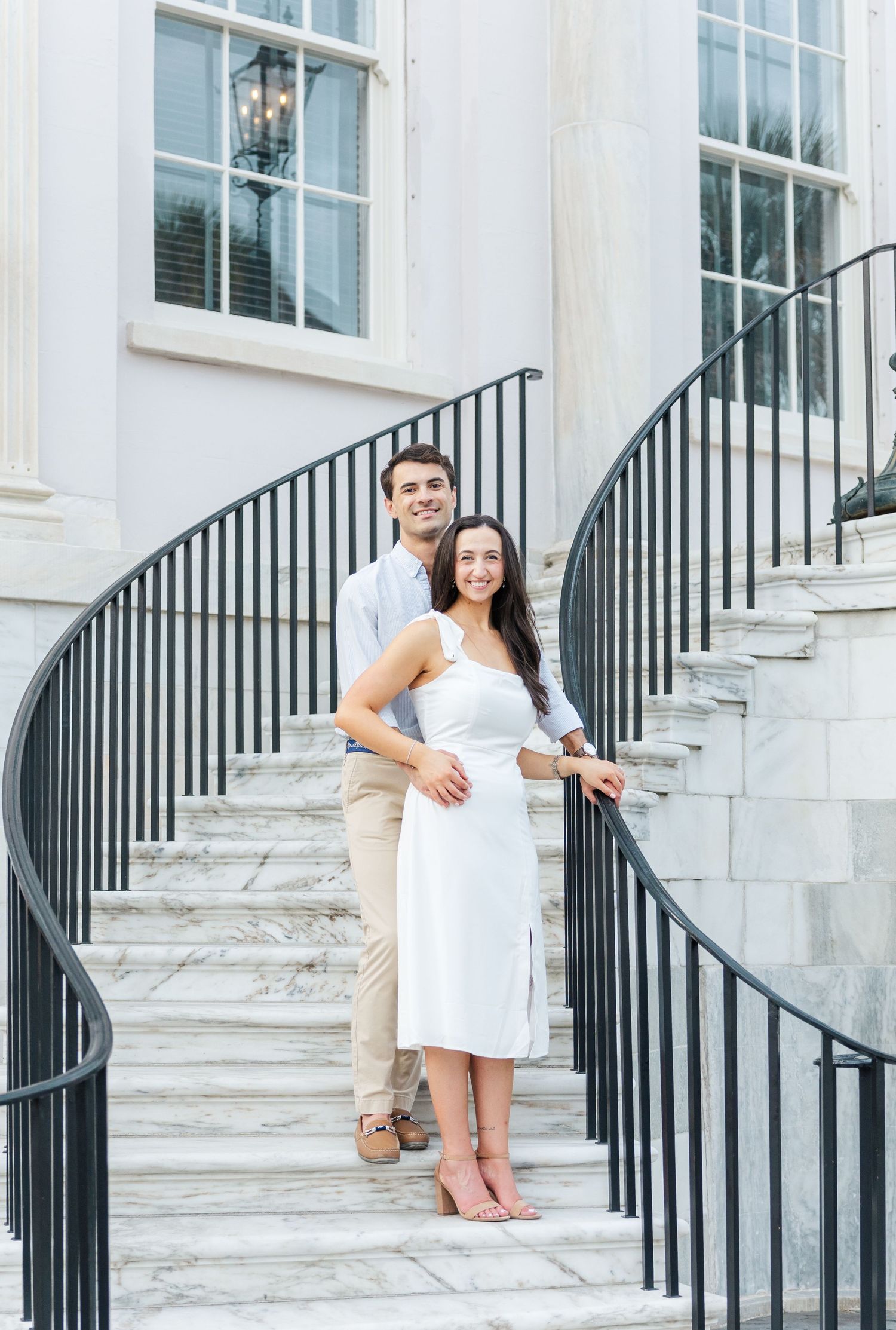 A couple posing on elegant curved marble stairs outside a classic white columned building.