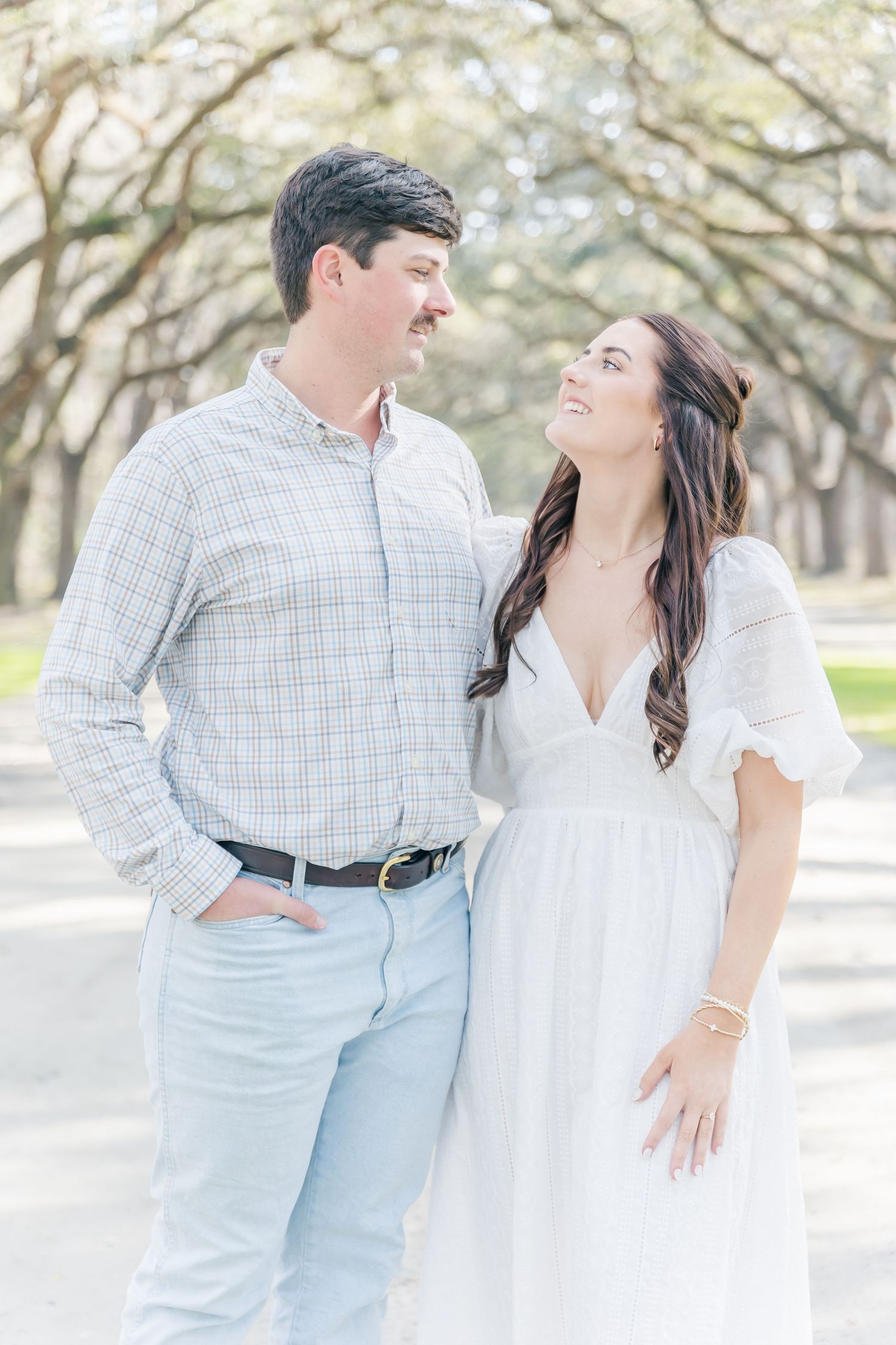 A couple shares a loving look while posing on a tree-covered path.