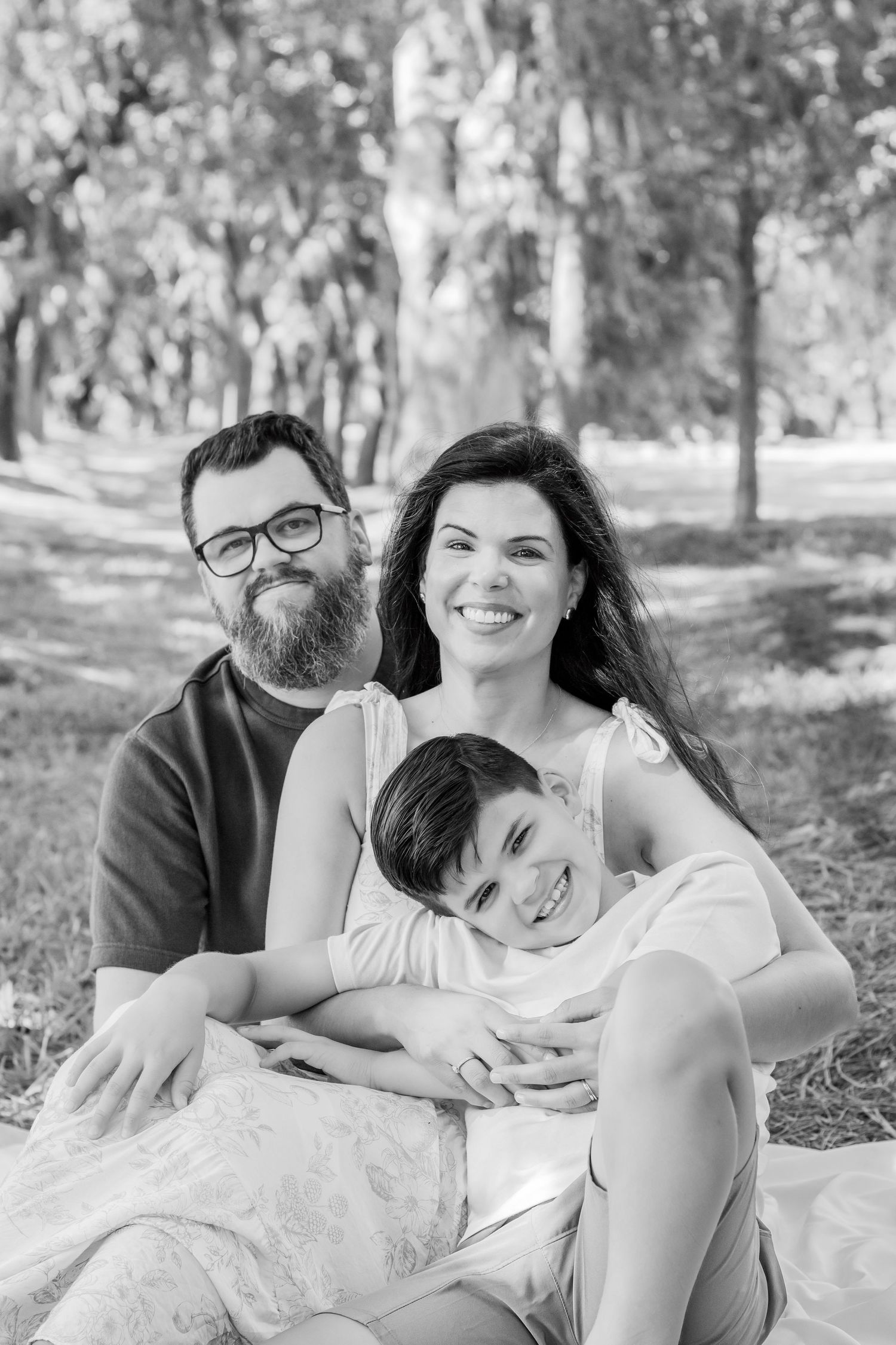 A family sits together on a blanket in a black and white portrait under oak trees.
