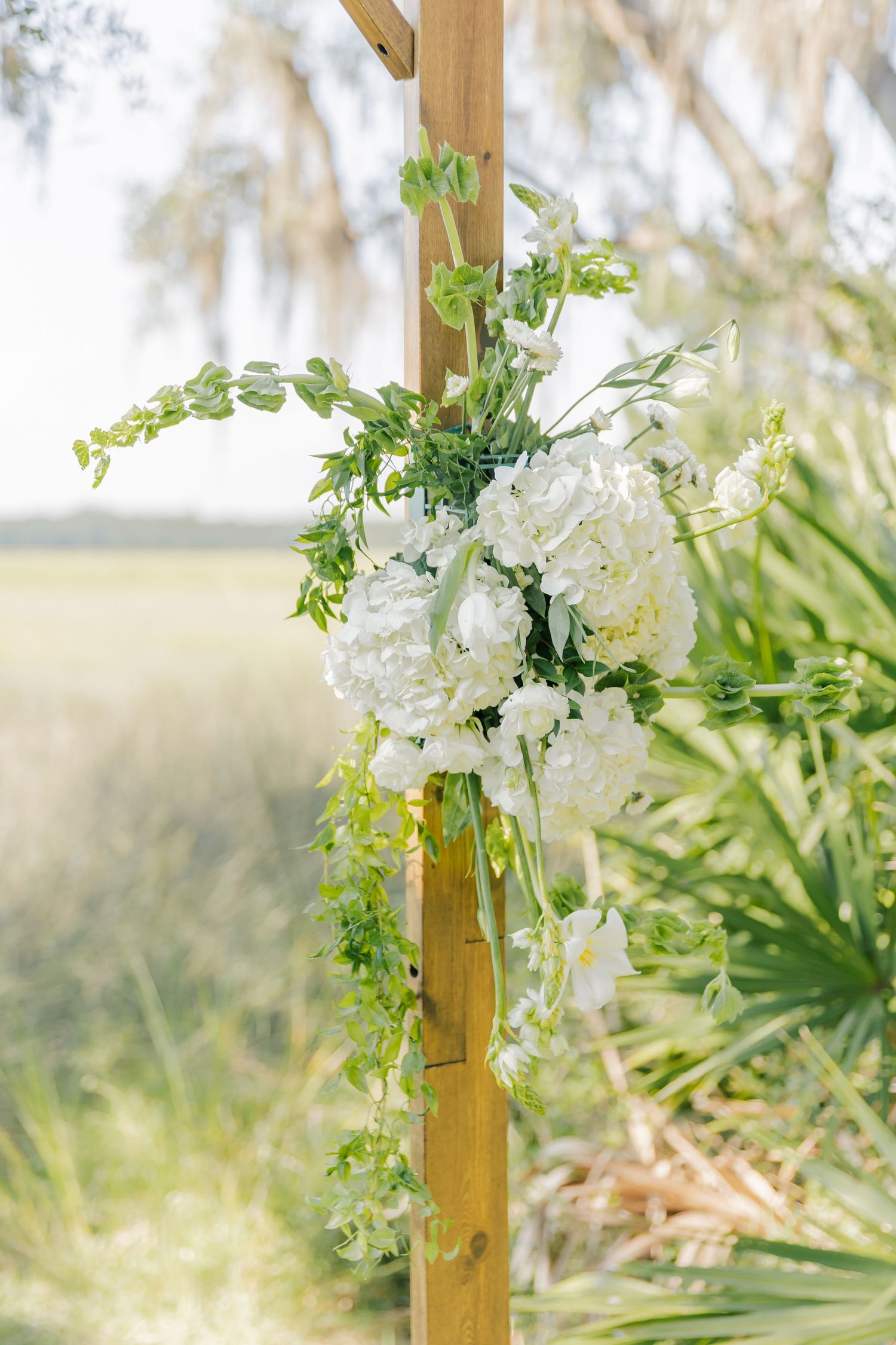 White floral arrangements with greenery adorn wooden posts in an outdoor garden setting.