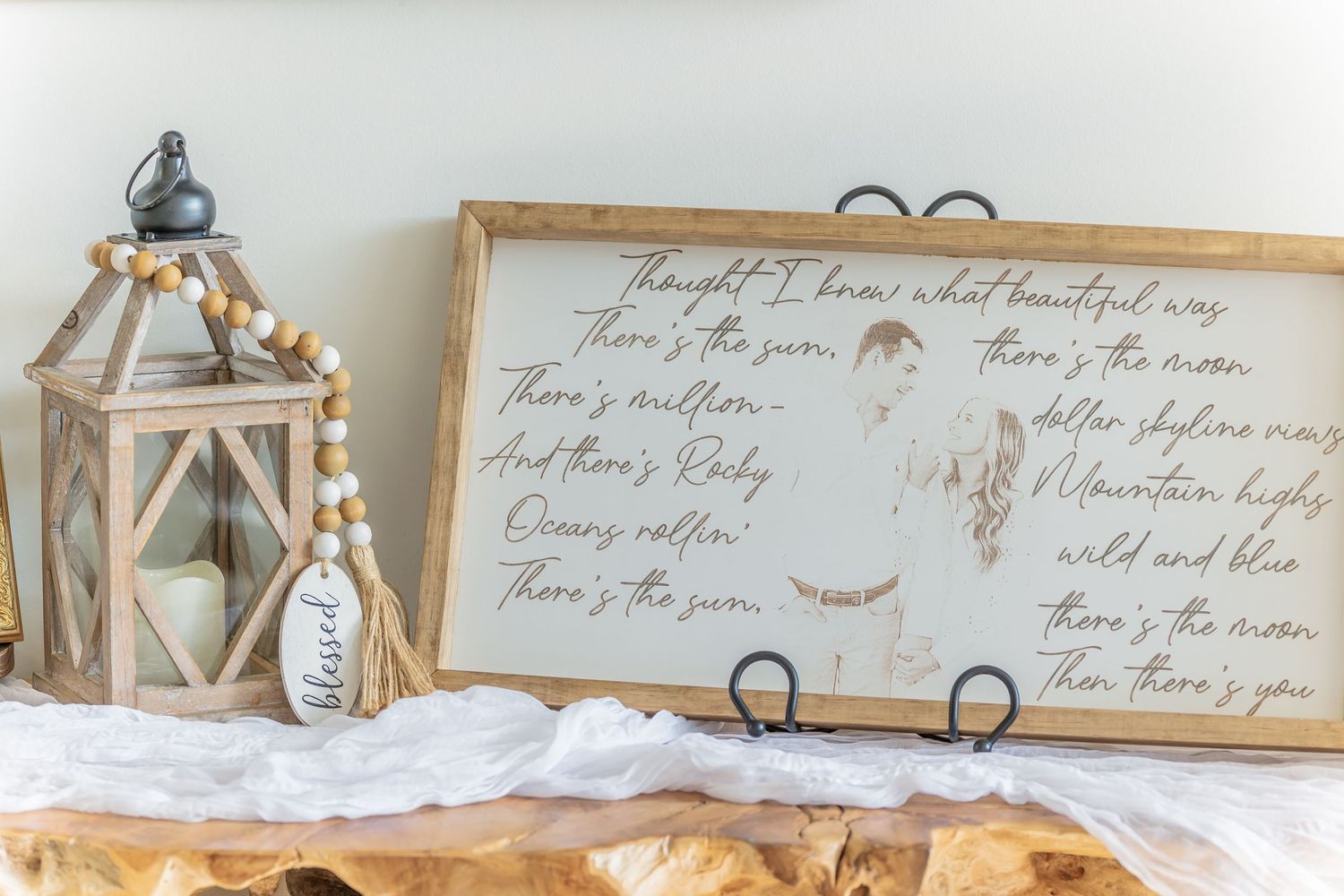 Rustic farmhouse decor featuring a wooden lantern and framed cursive text on display against a white wall.