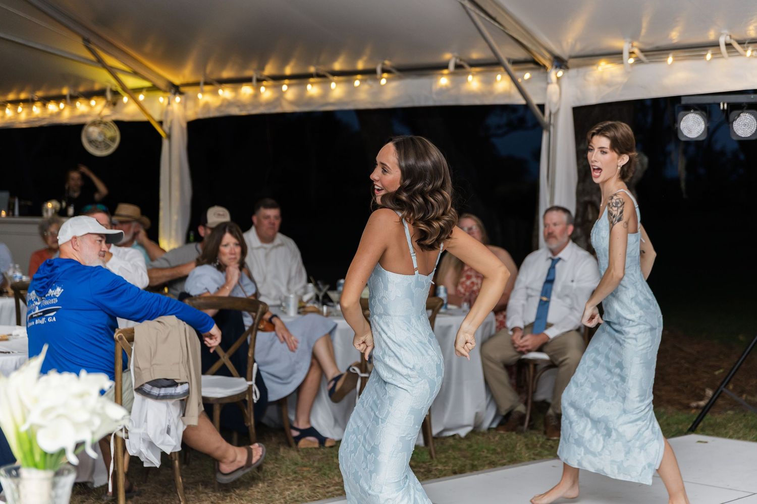 Wedding celebration under a tent with string lights creating a festive atmosphere.