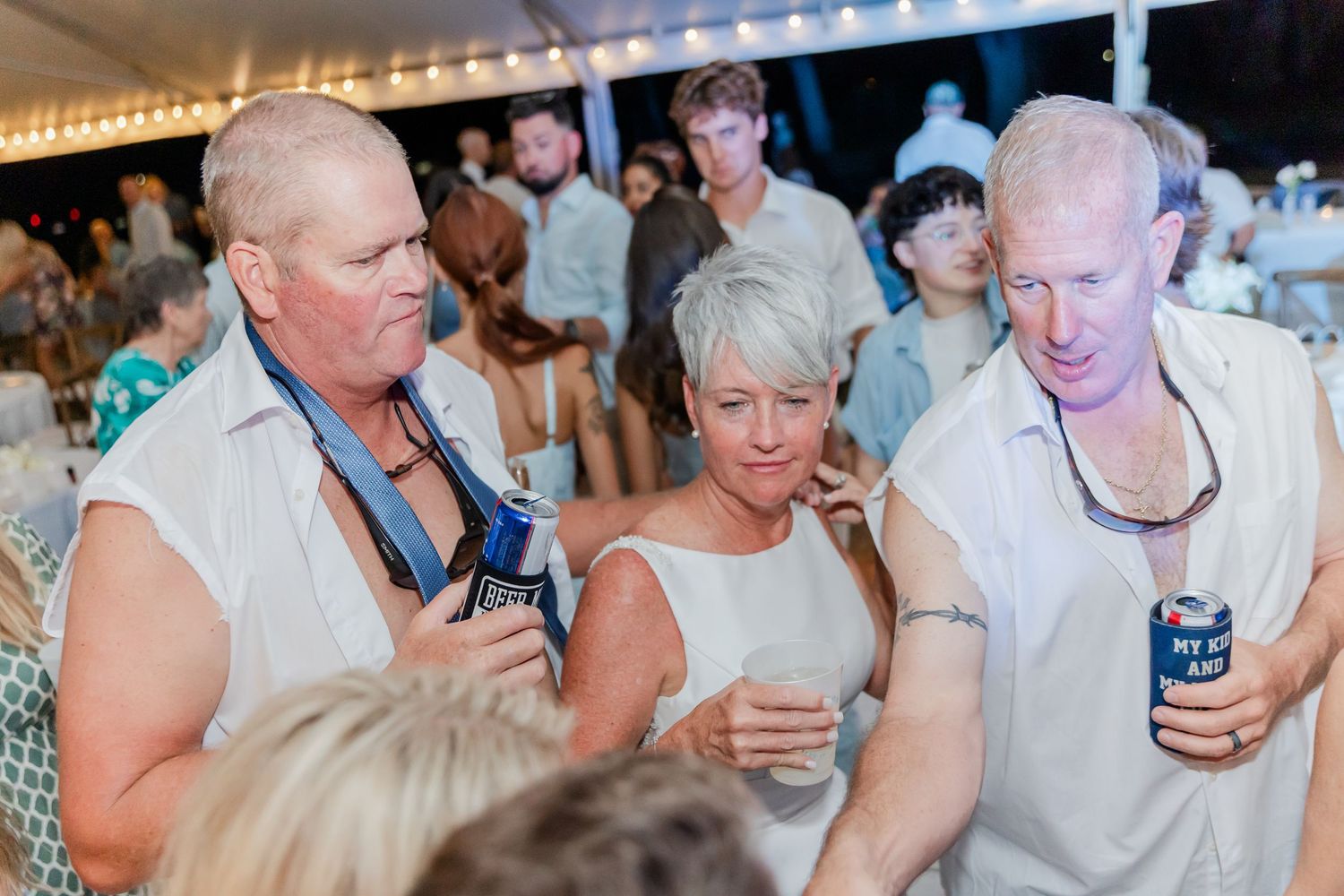 Wedding guests mingle and socialize during a lively reception celebration under a tent.