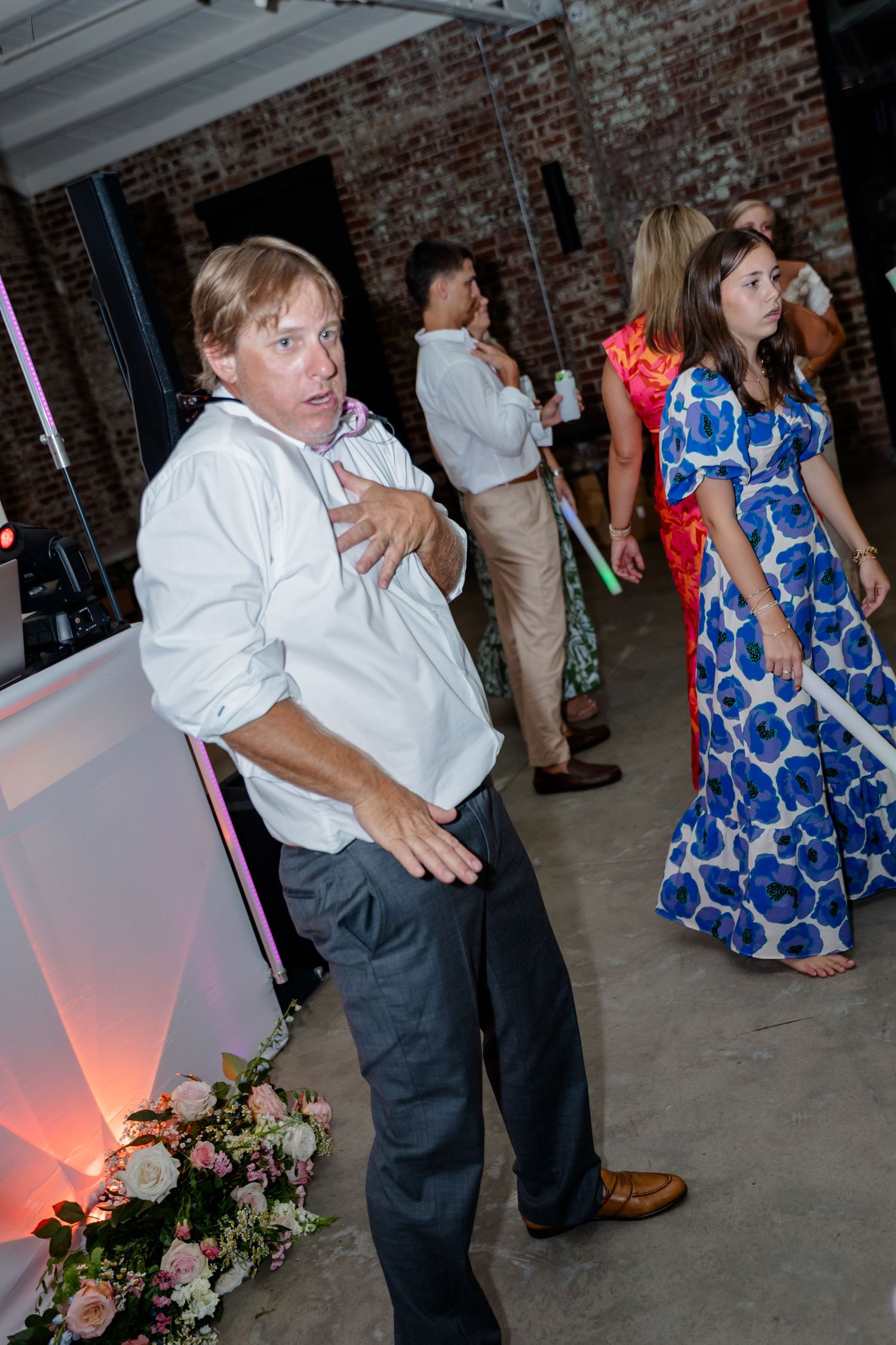 Wedding reception guests dance and celebrate on the dance floor beneath exposed brick walls.