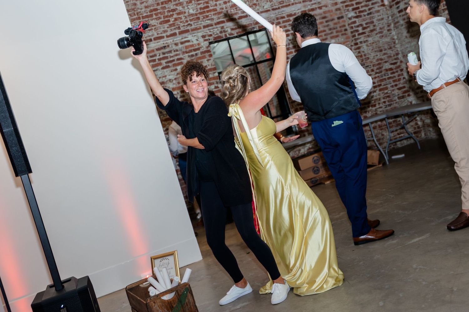 Wedding guests dance and celebrate on a rustic brick-walled dance floor during a reception celebration.
