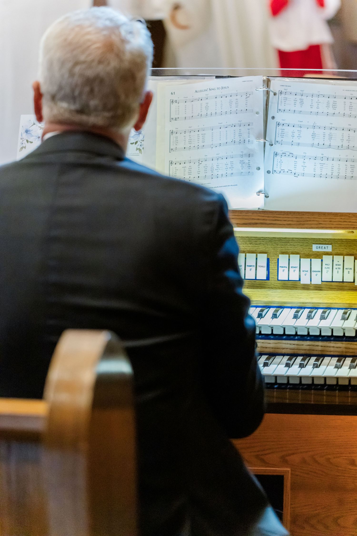 Piano sheet music in focus with blurred church pews and attendees in background.